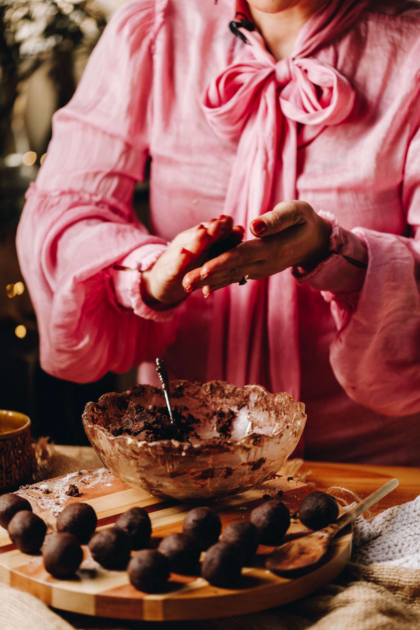 On a wooden table sits chocolate cookie balls. Naomi Toilalo is rolling one in here hands too. A vintage bowl with remnants of cookie dough is also on the wooden board. 