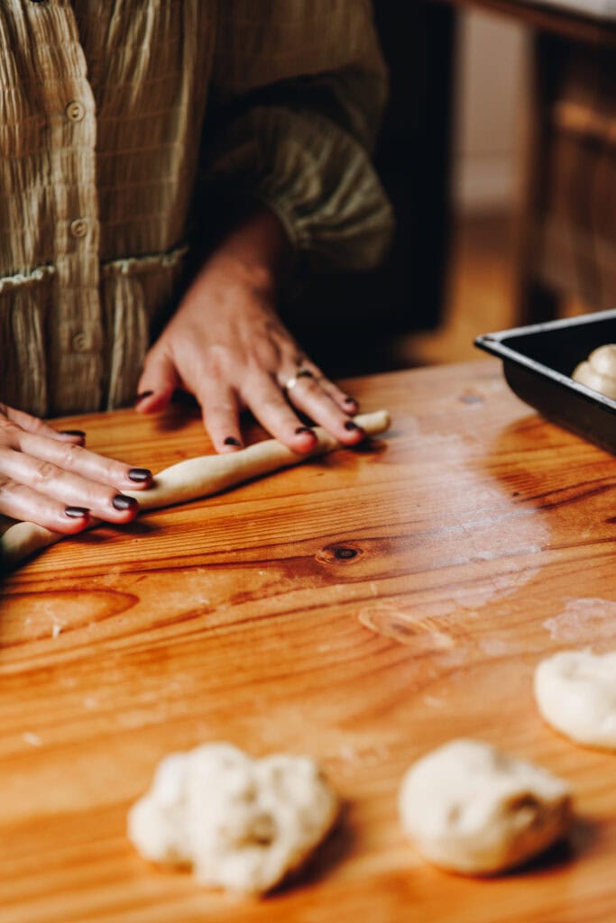 On a wooden table, Naomi's hand are rolling out the dough in to a sausage shape to make the Coconut Buns (Pani Popo)