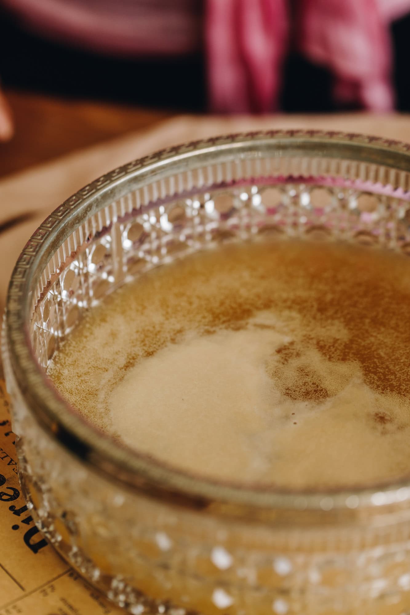 A bowl of activated yeast sits on a wooden table. The yeast is lightly foamy and rising to the top of the water.