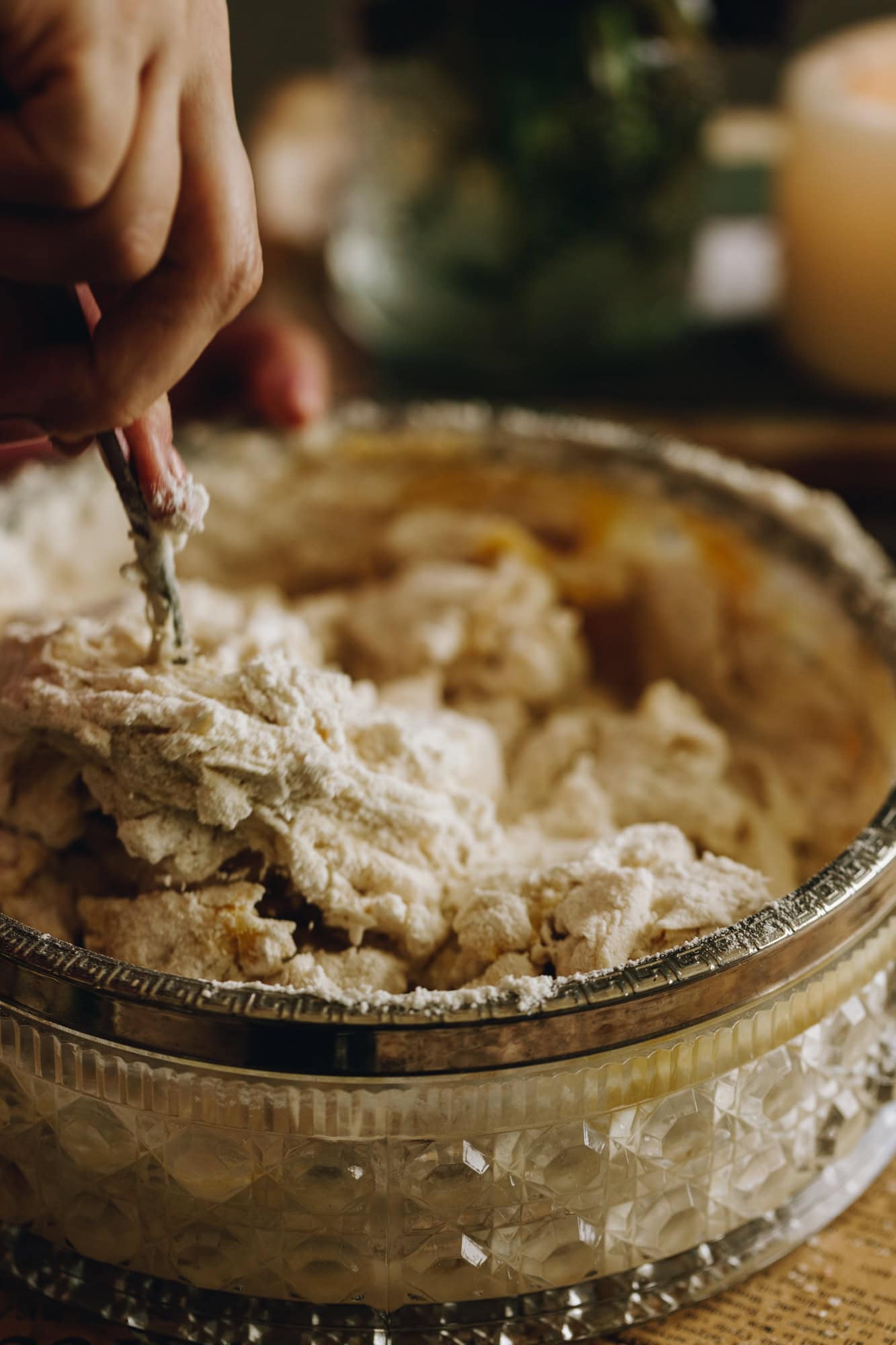 A hand is mixing together the ingredients of the no-white bread loaf in a vintage bowl with a silver trim. It is on a wooden table.