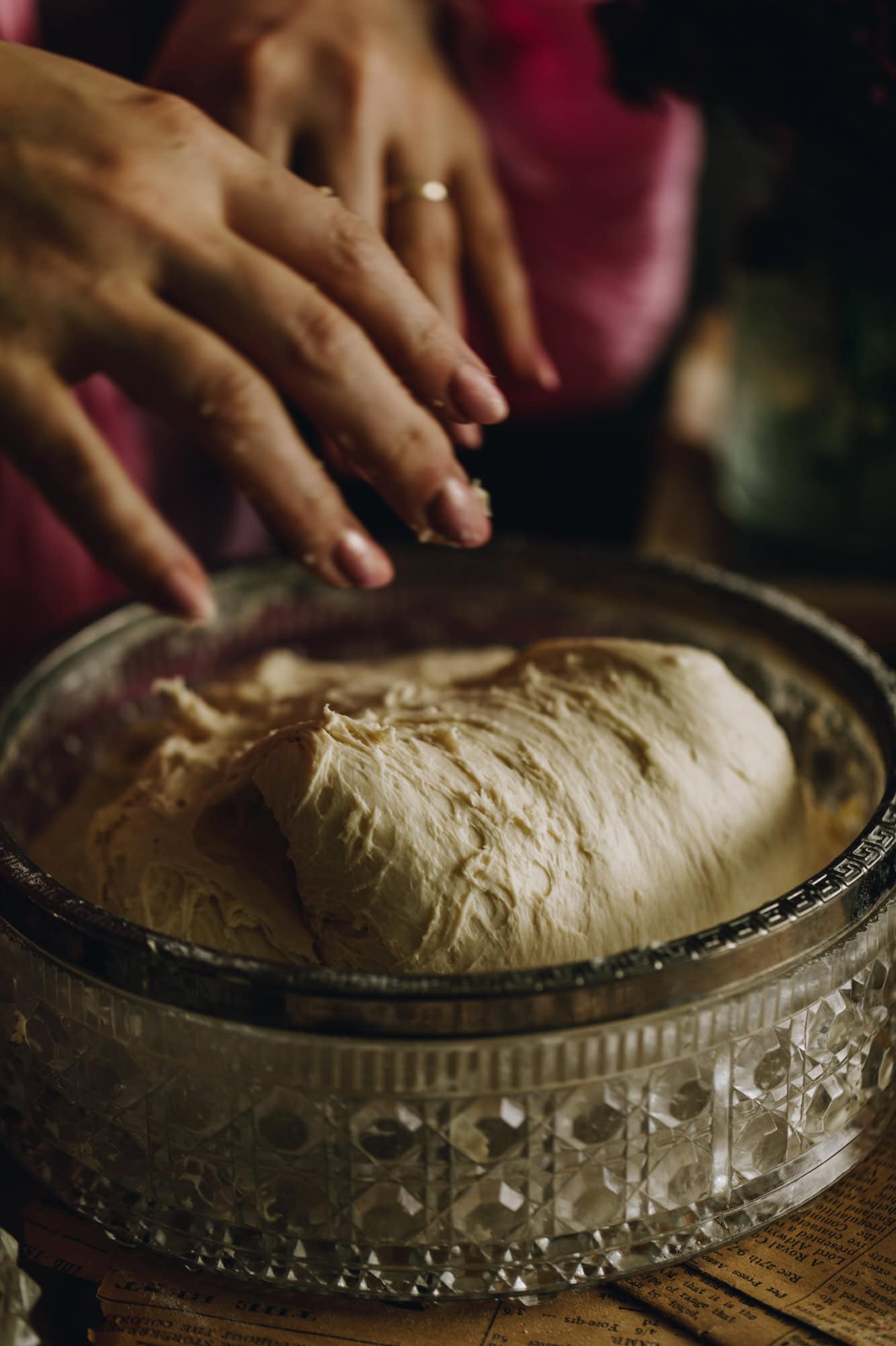 The dough is in a bowl, a hand is reaching in to grab it. 