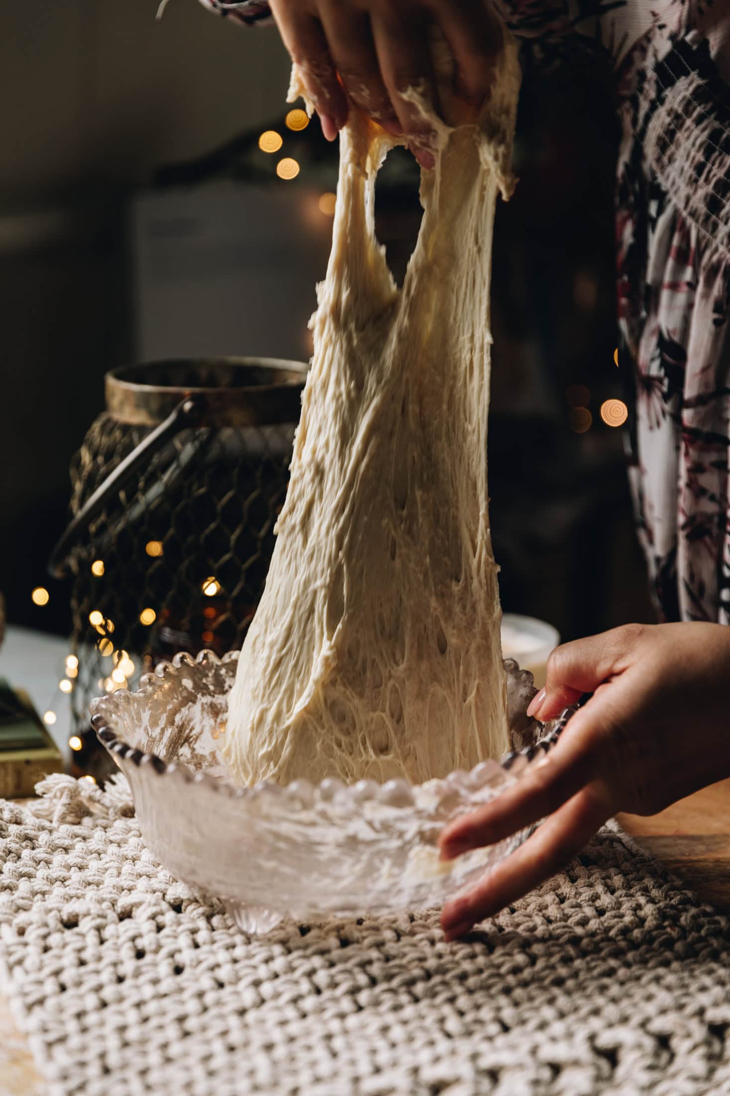 A hand is gathering the dough of the rustic no-knead white bread loaf stretching the dough. The dough is being lifted high in the air.