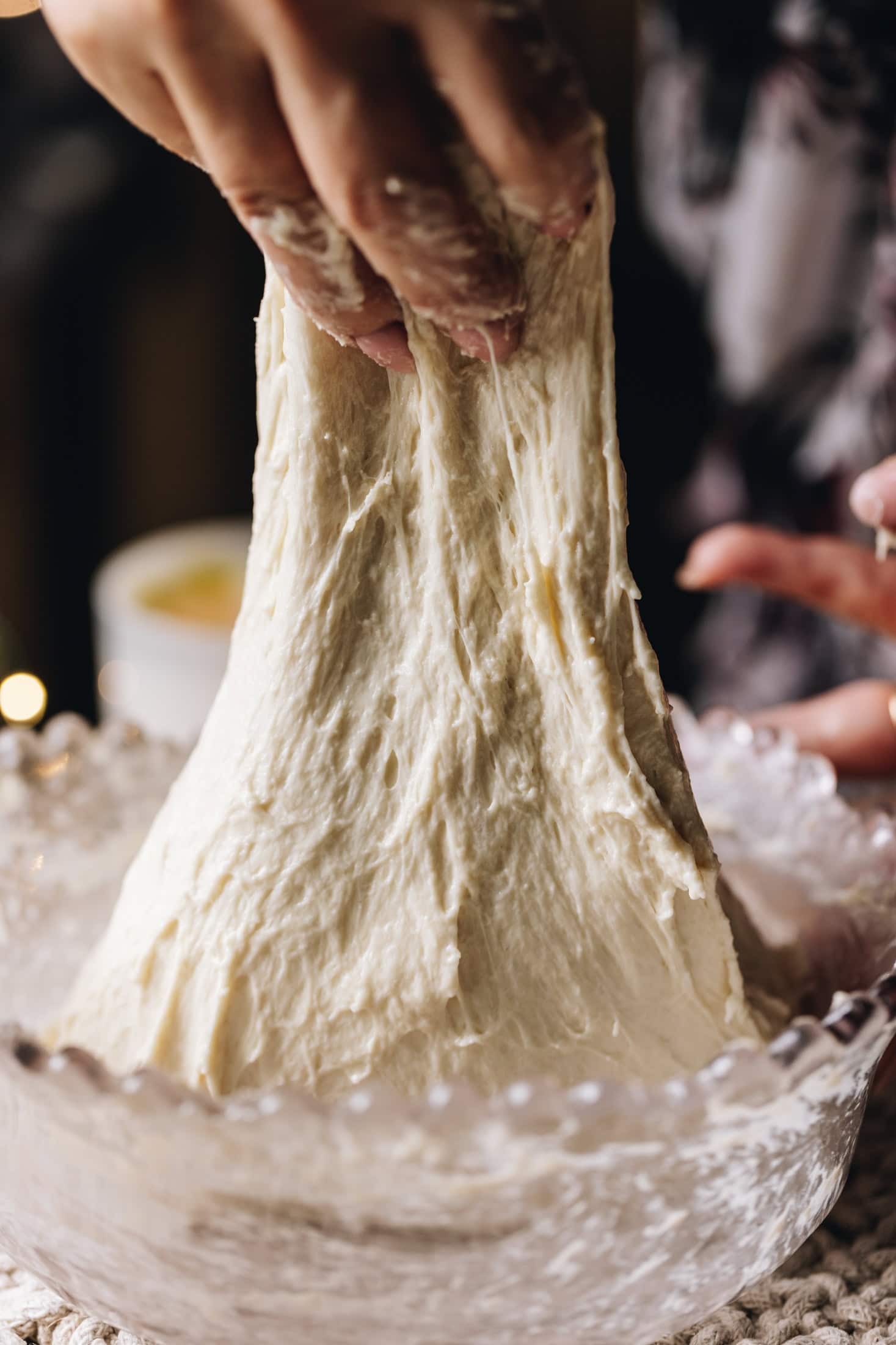 A hand is gathering the dough of the no-knead white bread loaf stretching the dough. The dough is being lifted high in the air.