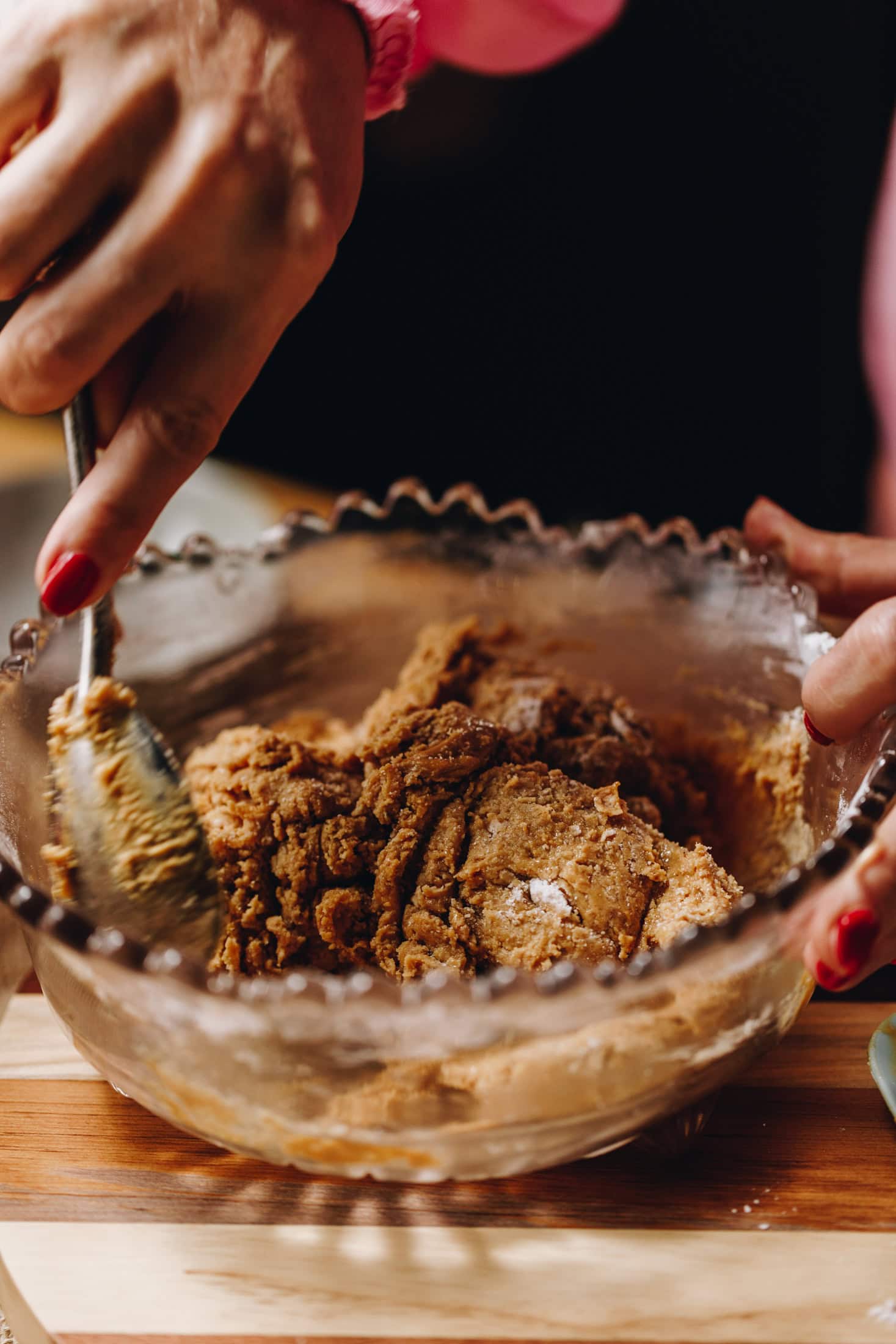On a wooden board sits a purple vintage bowl. In it is the peanut butter buckeye truffle mixture that is being stirred by Naomi with a vintage spoon.