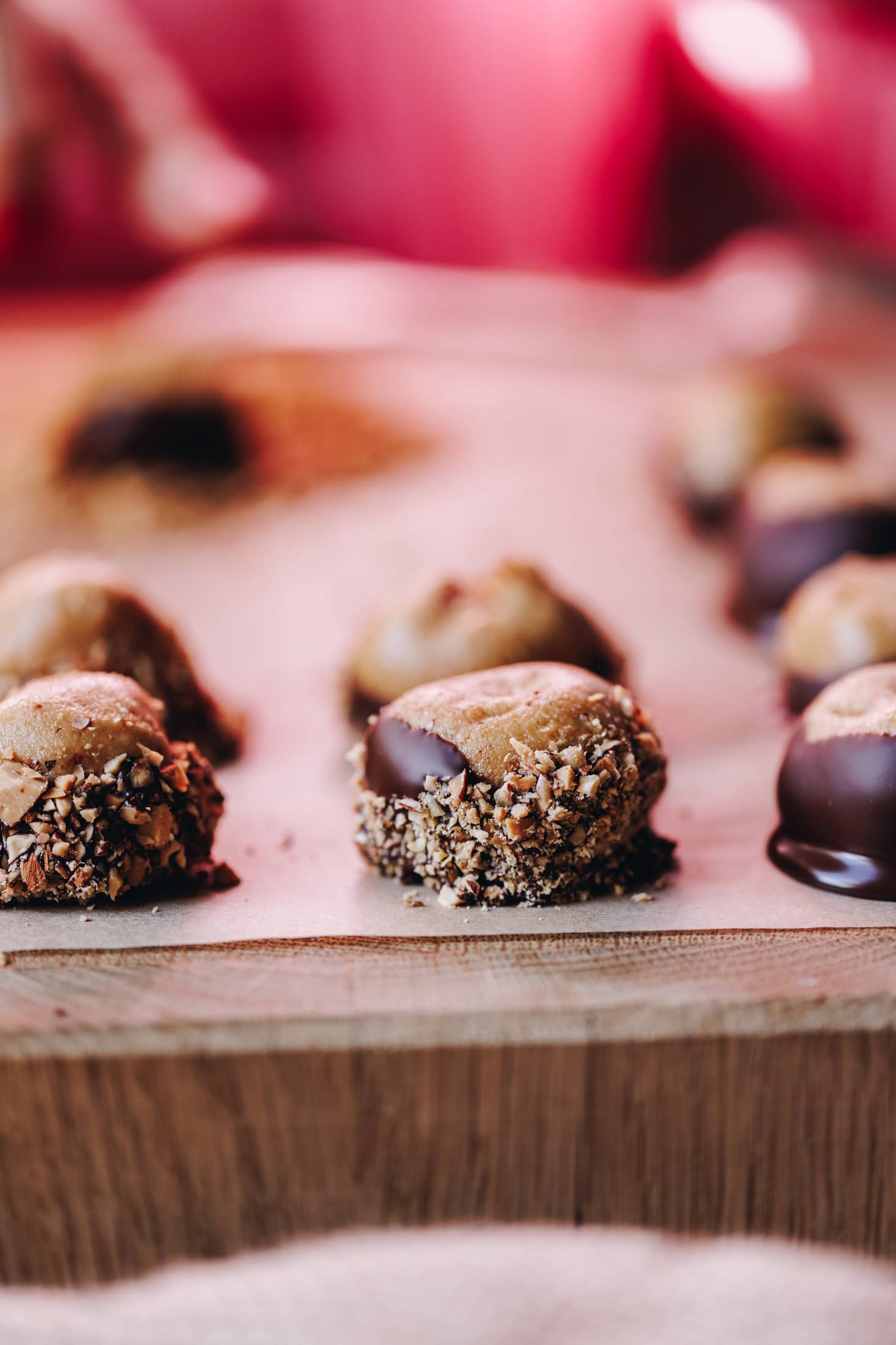 On a wooden board sits a large piece of baking paper with freshly dipped peanut butter buckeye truffles. These ones have crushed nuts on them as well.
