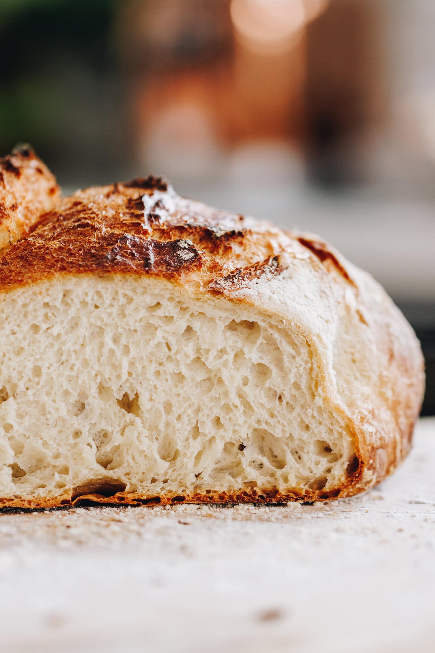 A freshly baked Rustic No-knead Bread Loaf has been cut open, it shows the crusty crust and soft interior. It is on a floured table. 