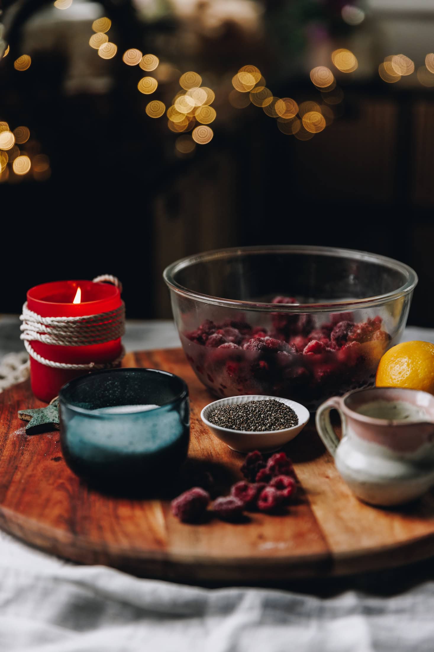 The Chia Raspberry and Lemon Jam ingredients
are in different vintage bowls and are sitting on a wooden board. A red candle are behind the ingredients.