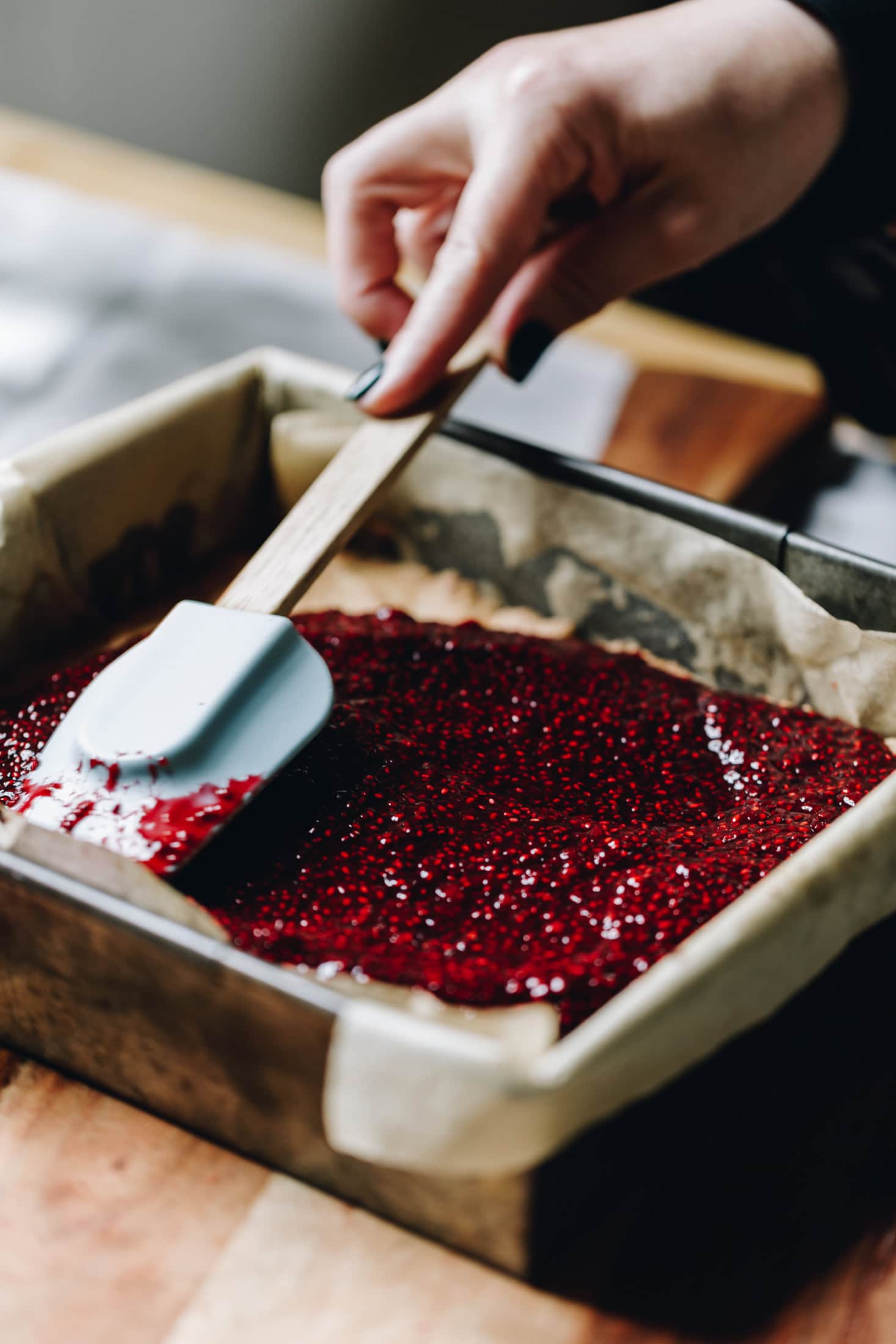 Chia raspberry and lemon jam is being spread over the hot Louise Cake Slice base.