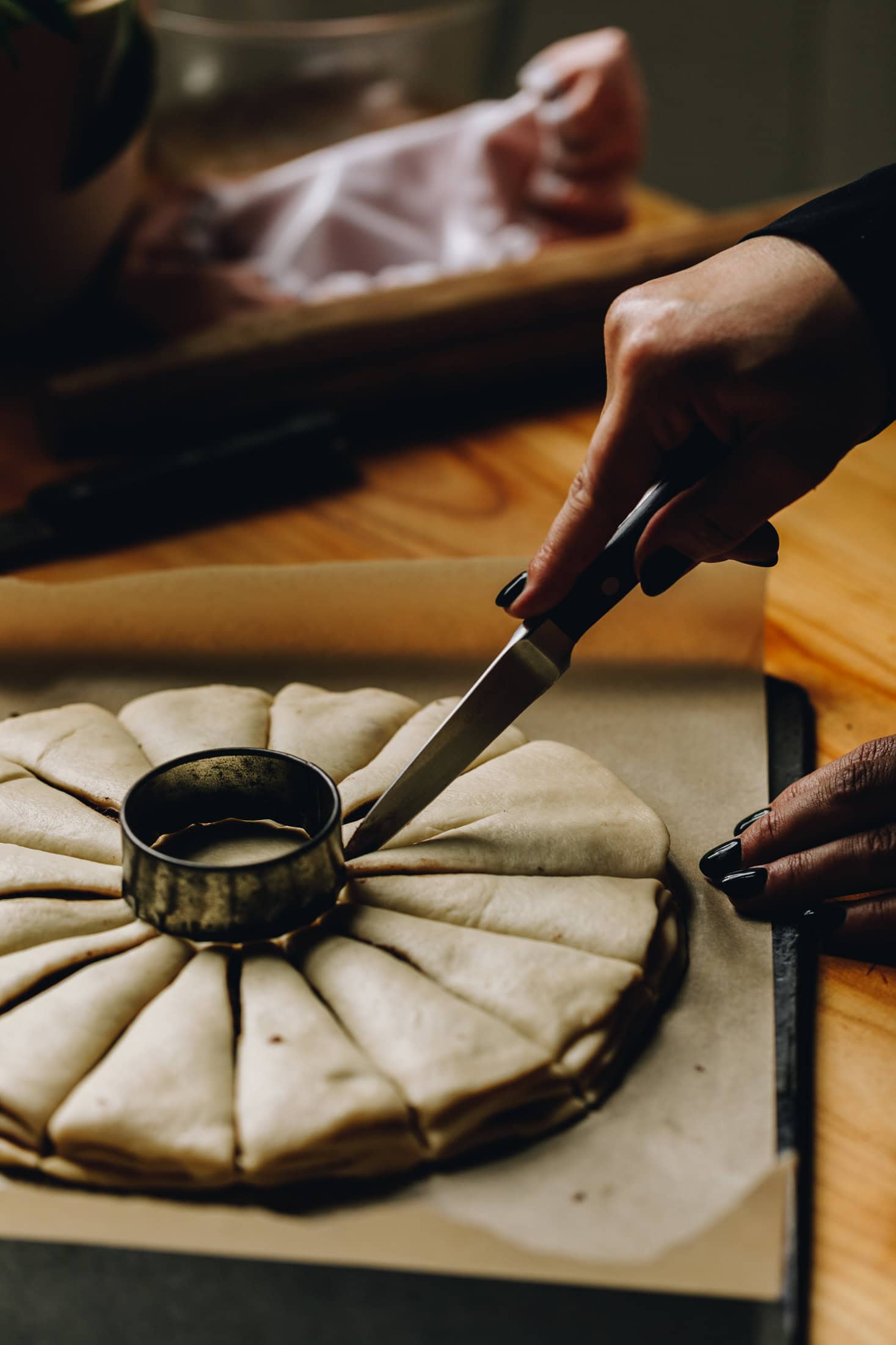 An unbaked Chocolate Star Bread is being cut in to 16 pieces. It is on a black tray with brown baking paper and is on a wooden table. 