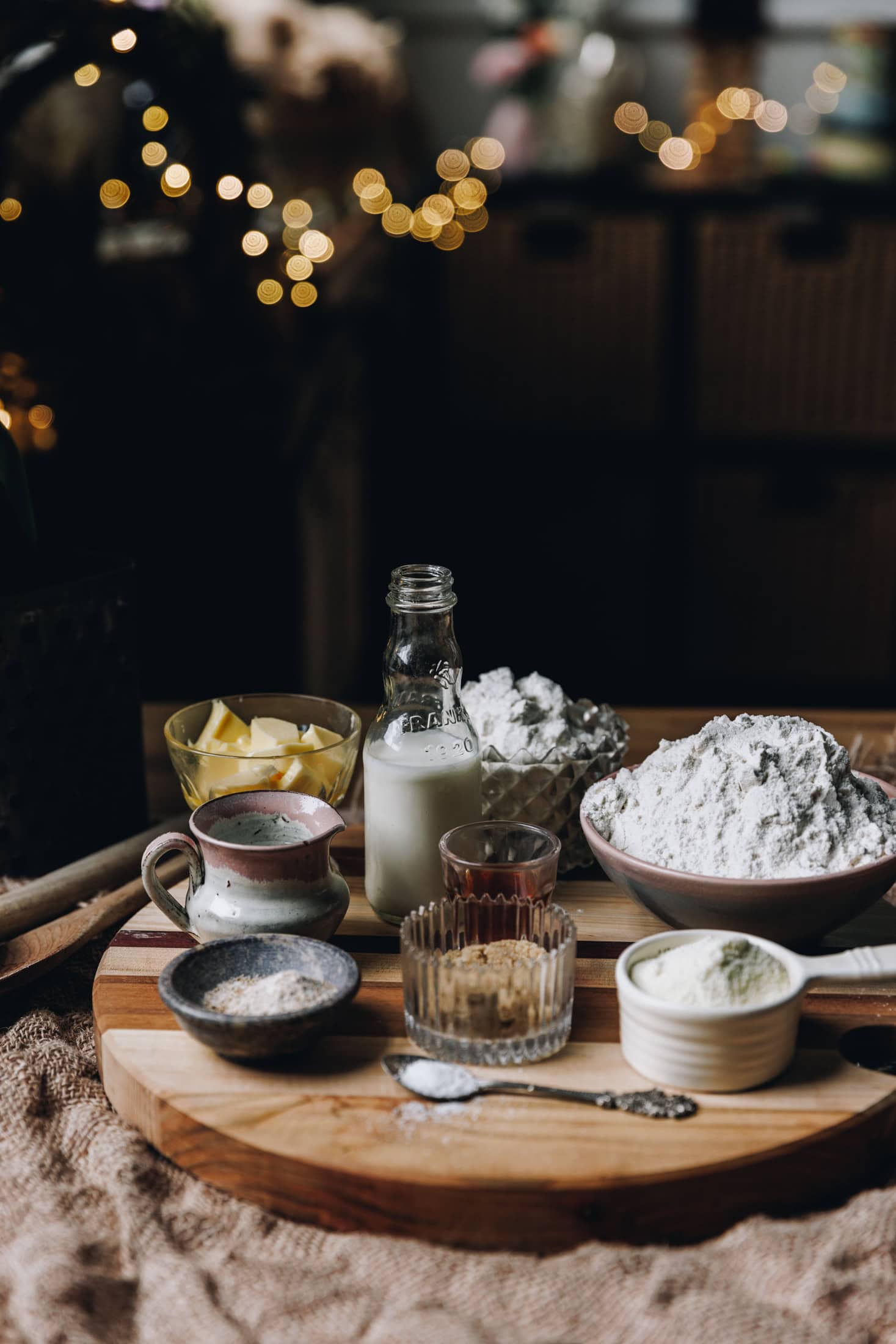 Chocolate Star Bread ingredients are in different vintage bowls and are sitting on a wooden board on top of wooden table. Fairy lights are in the background. 