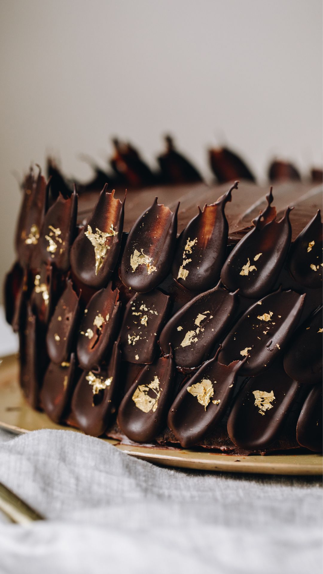 A wooden board sits on a brown stone bench. On the board is the tip of a sharp knife and dark chocolate that has been cut in to shards. 