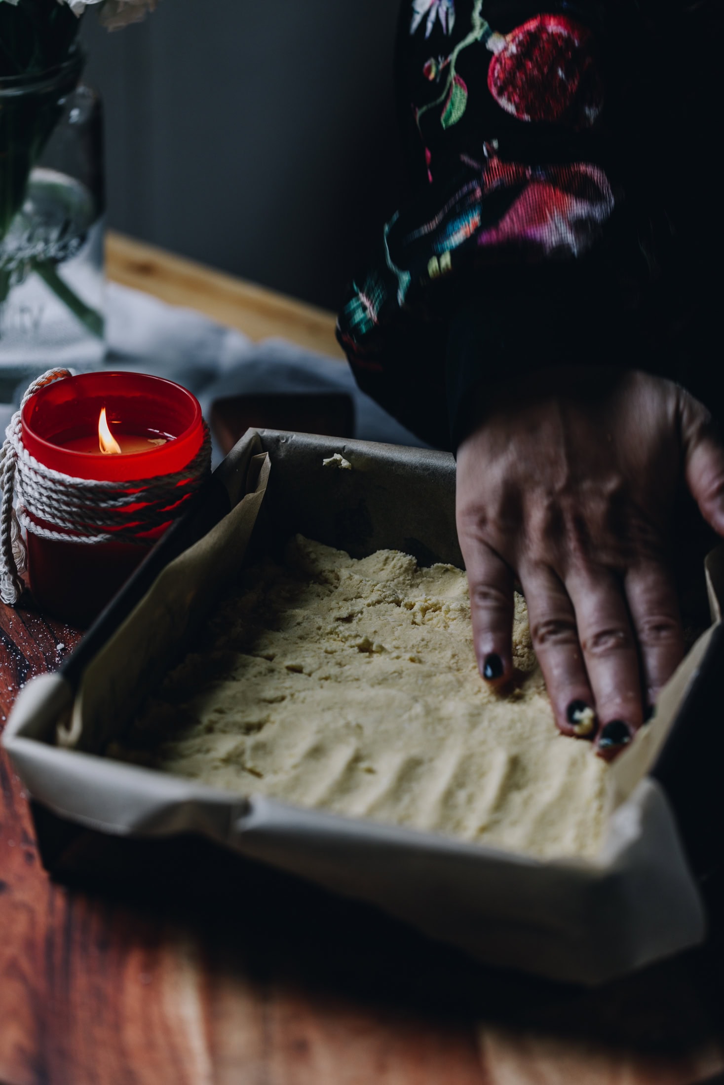 The Louise Cake Slice is pressed in to the base of tin, Naomi's hands are pressing the base down. It is on a wooden board. 