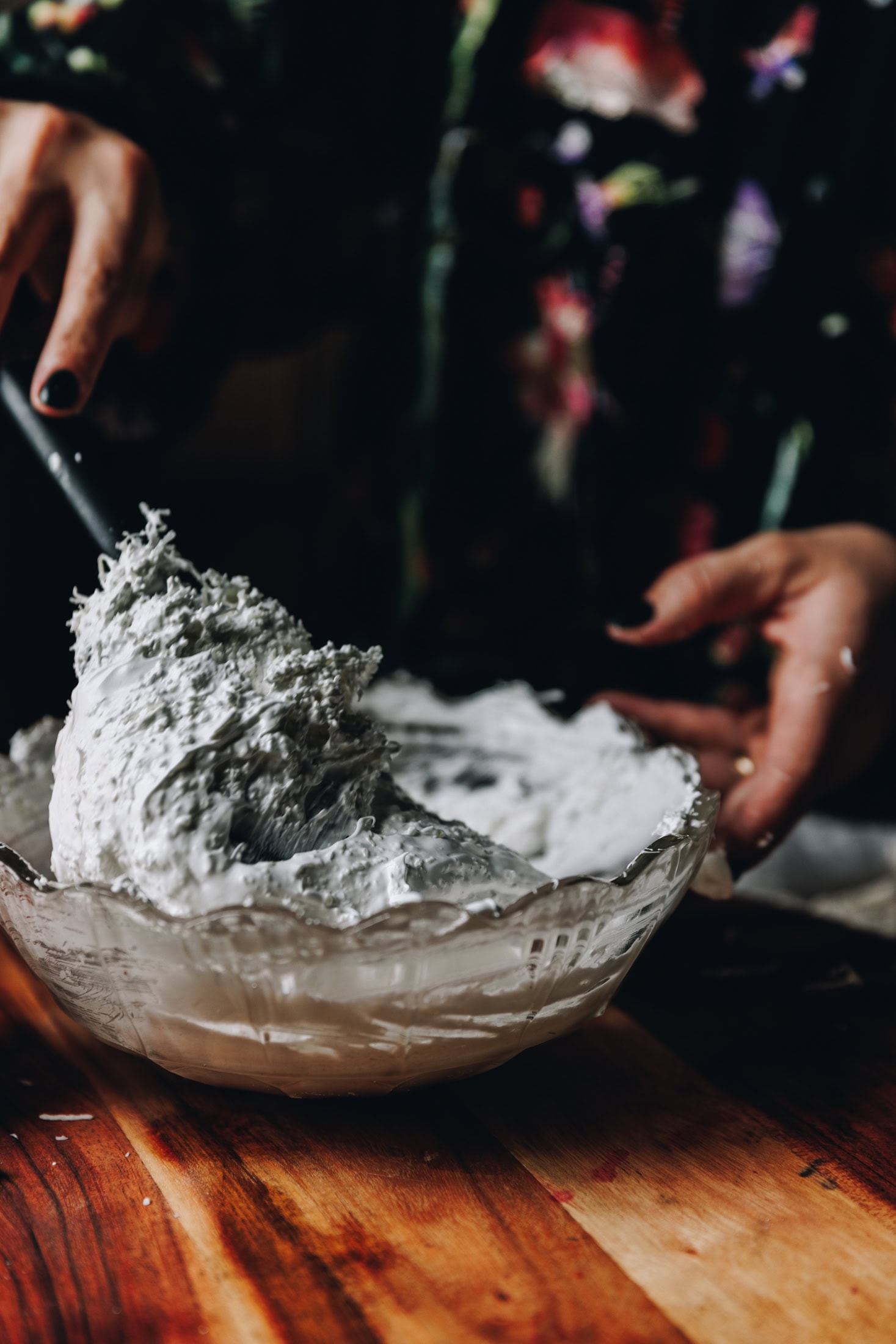 The coconut meringue for the slice is being folded together in a glass vintage bowl that is sitting on a wooden board. 