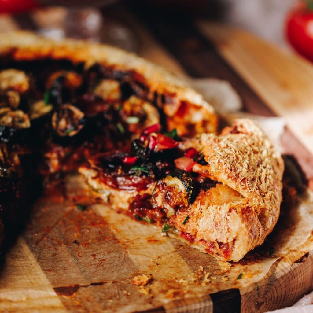 A slice of roasted tomato and courgette galette reveals the vegetables inside the rustic pastry.