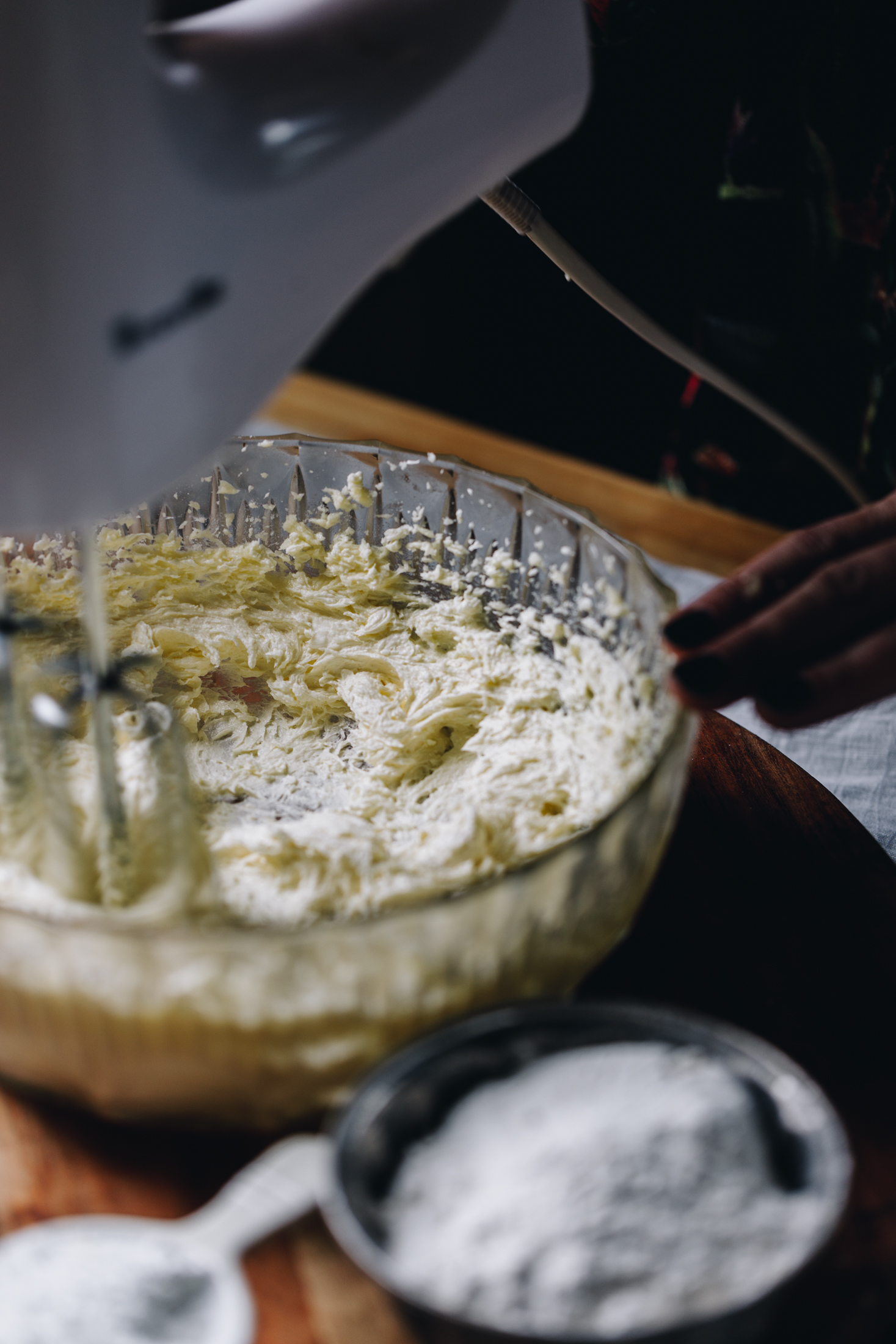 The butter and sugar is being whipped together in a glass bowl that is sitting on a wooden board. 