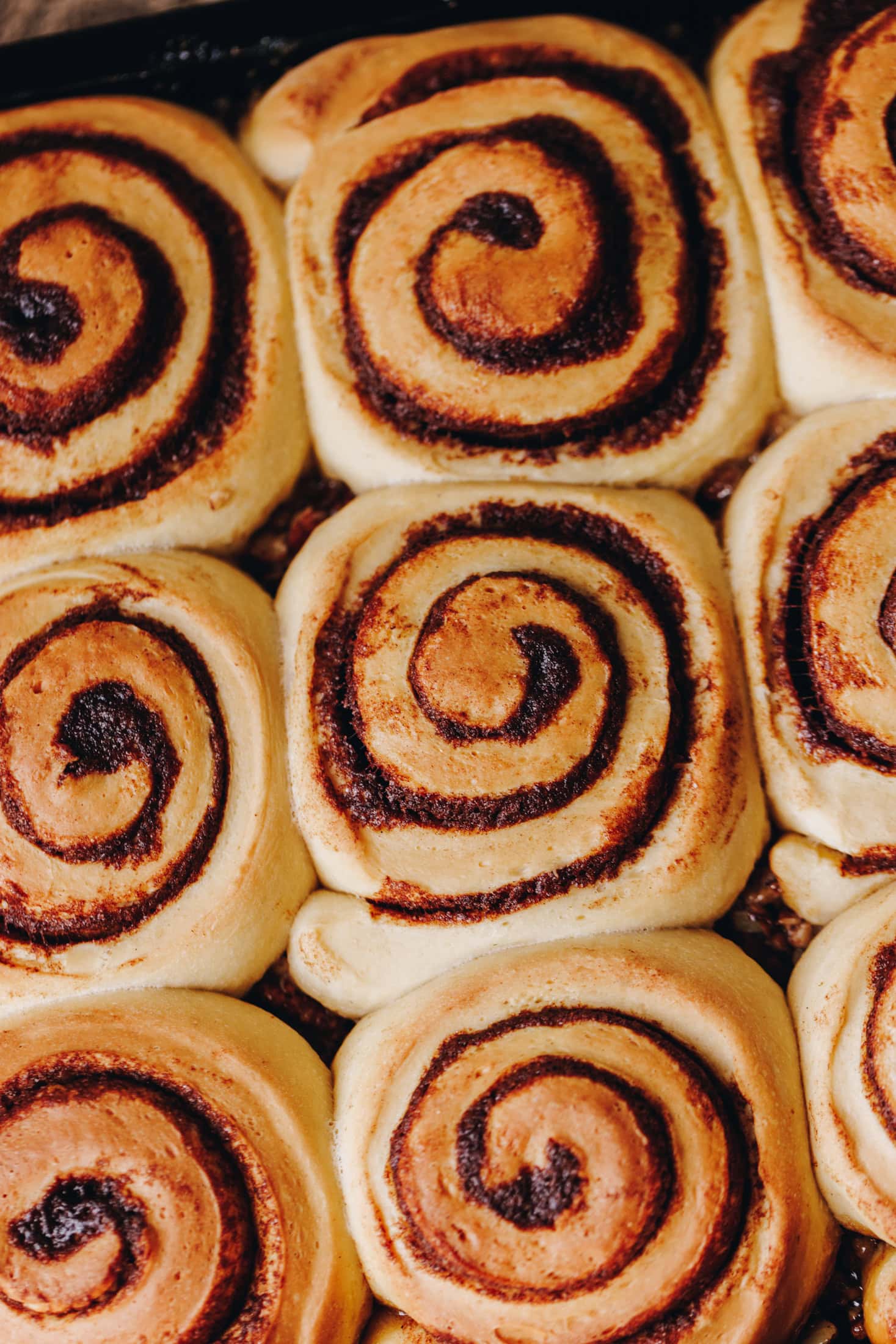 A flat lay shot shows a tray filled with baked sticky maple cinnamon scrolls. The dough has spirals of cinnamon butter in seen baked in to the dough but the caramel is not seen. The scrolls have not been flipped over yet.