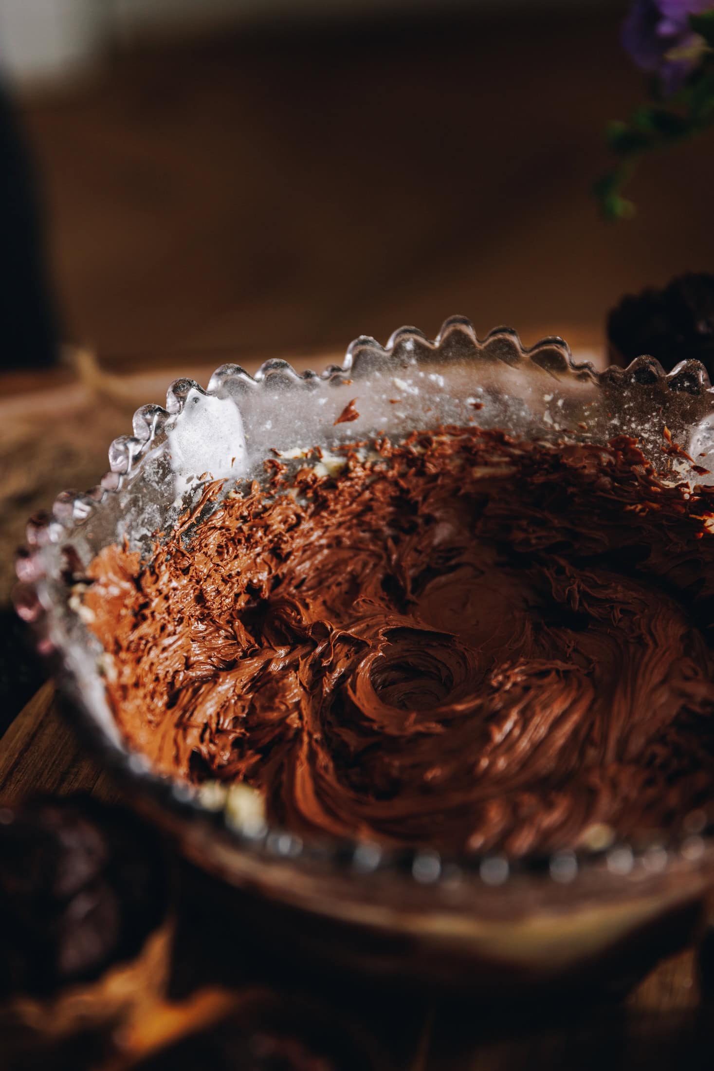 A purple vintage bowl is sitting on a wooden board. Inside the bowl is whipped dark chocolate buttercream.