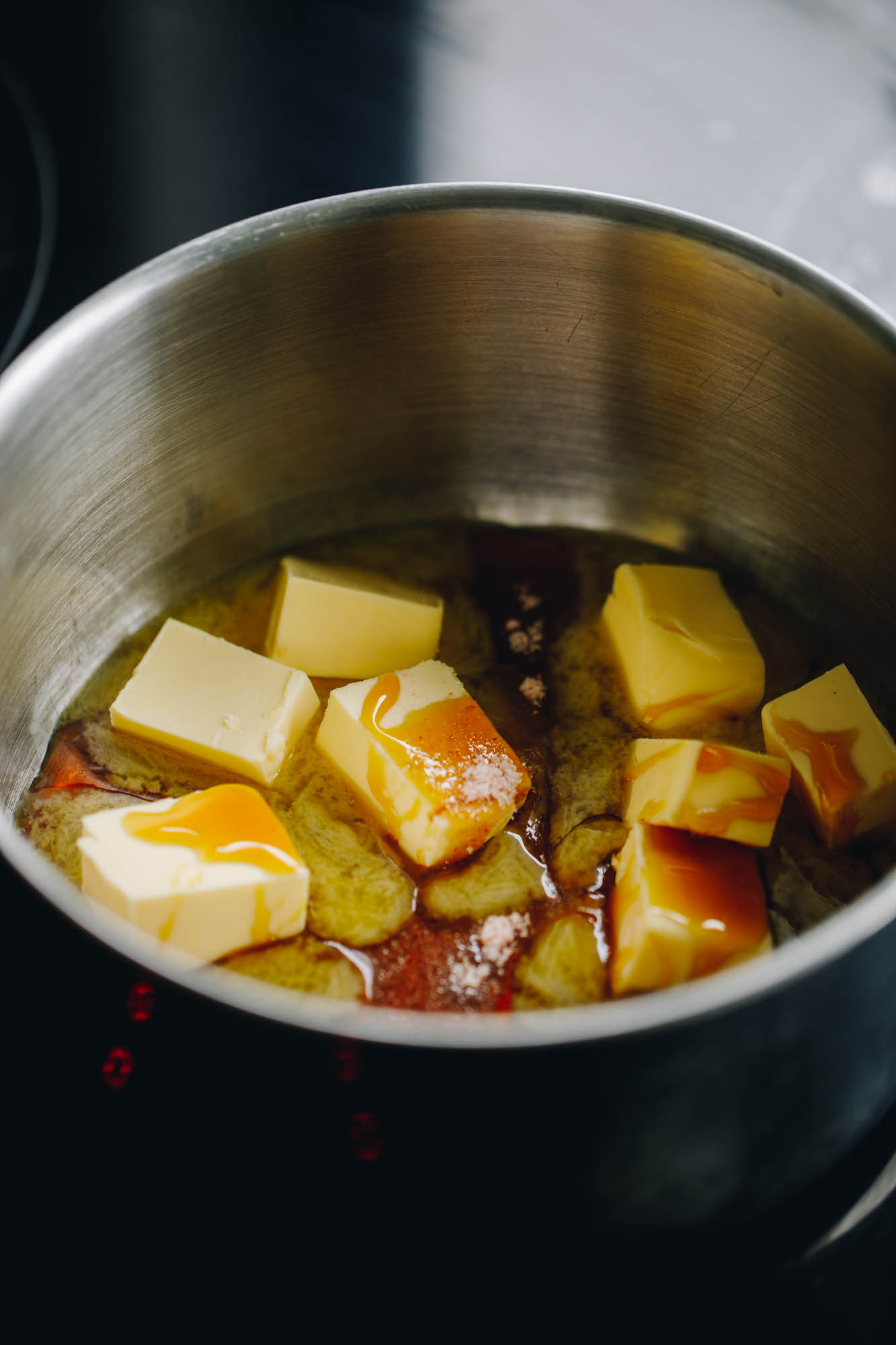In a silver pot is molasses and butter that is melting on a black stove. 