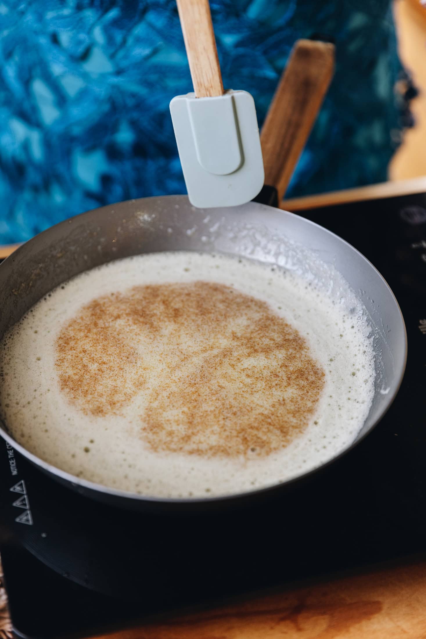 Brown butter is in a frying pan that is foaming and brown speckles have floated to the top, a spatula is suspended in the air ready to stir.