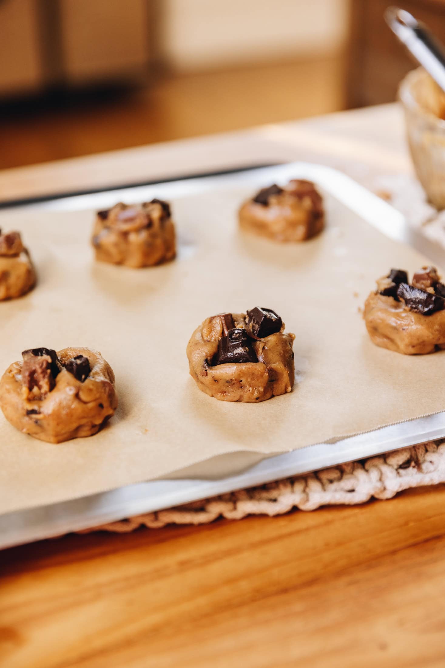 Unbaked brown butter chocolate cookies are rolled in to balls and have chocolate chunks in them. They are on brown baking paper on a silver tray that is on a wooden table.