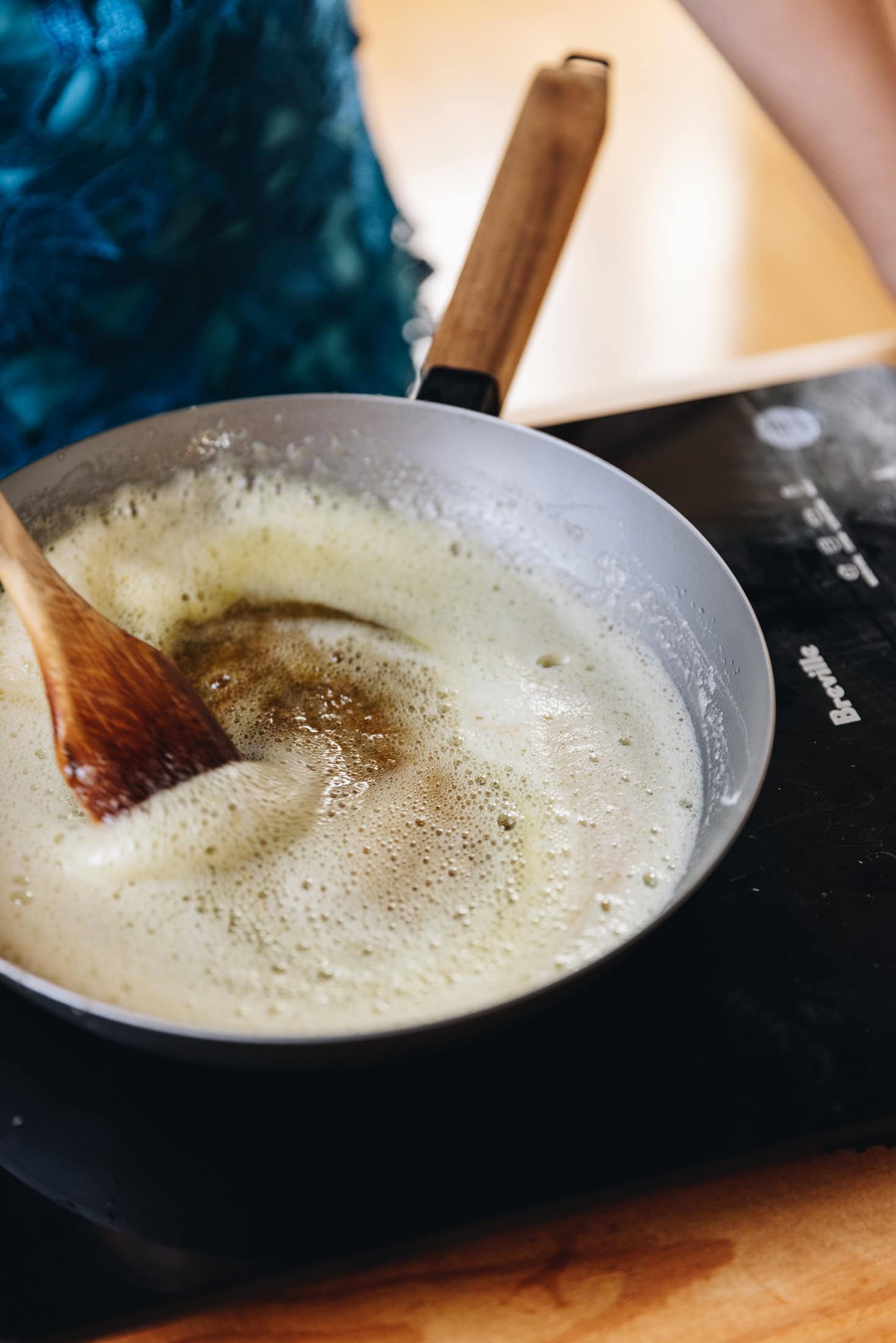 Brown butter is in a frying pan pan that is foaming and is being stirred by a wooden spoon. 