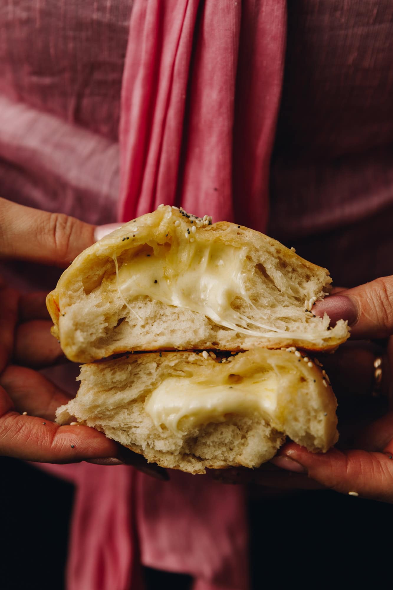 A close up shot of cheesy no-knead bread buns shows a bun cut open and the gooey cheese is oozing out of the centre.