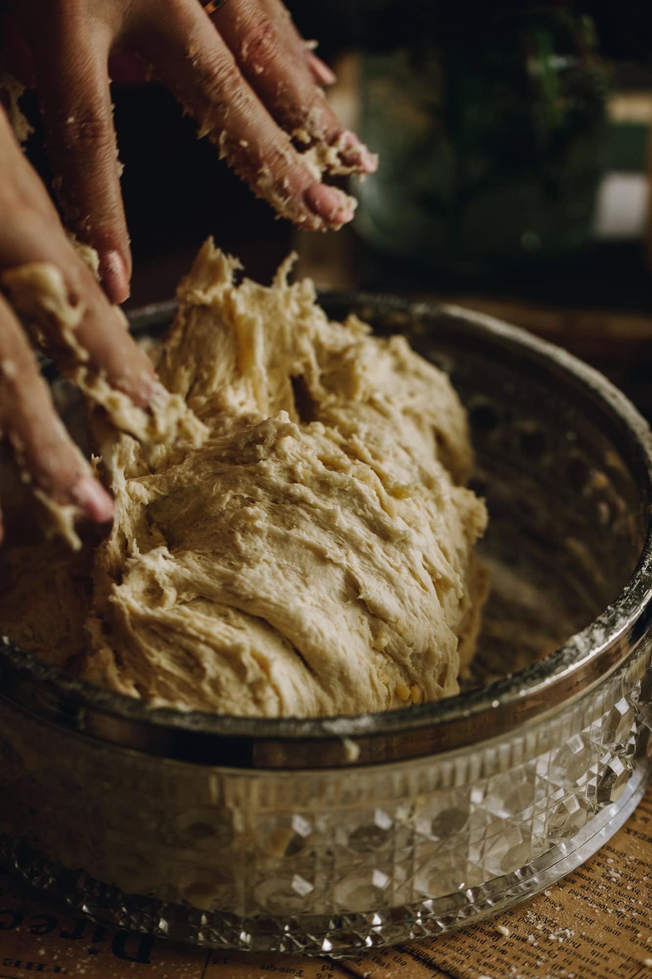 Sticky fingers are in a bowl of no-knead- bread bun dough. It is in a vintage glass bowl.