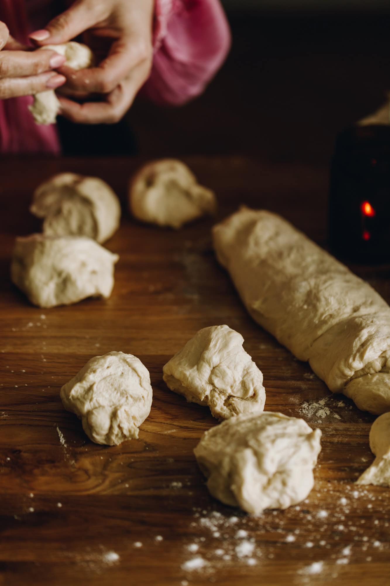 On a lightly floured table is pieces of dough, ready to be made in to a buns. 