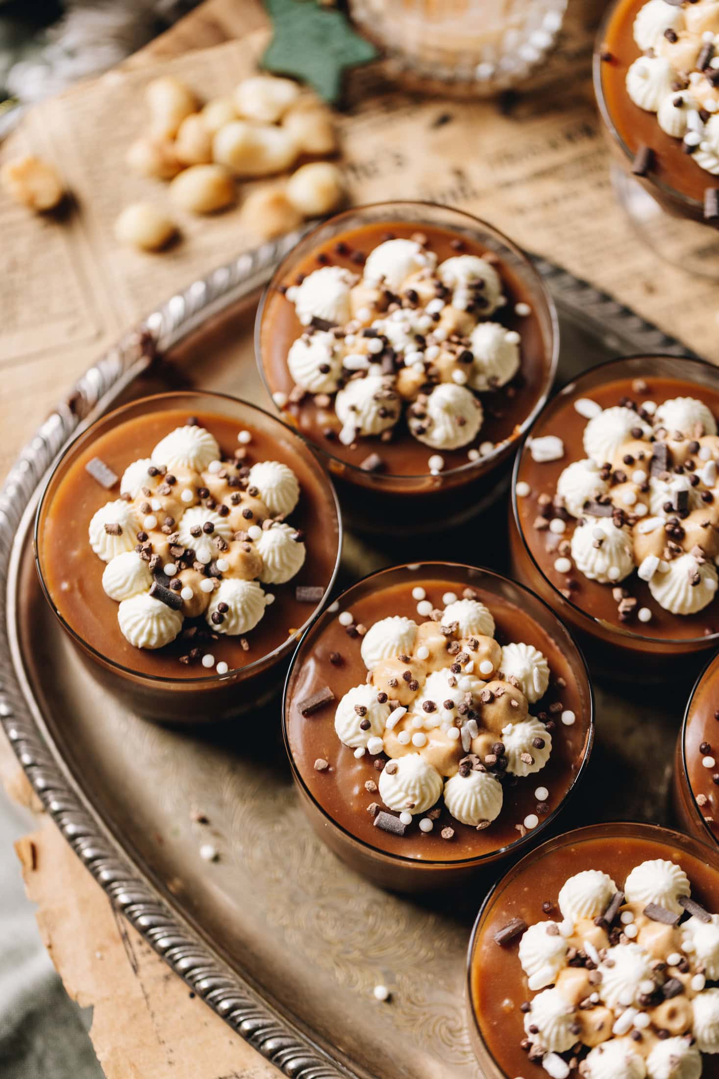 A top shot shows the homemade salted caramel sauce on top of decorated desserts in glass jars that sit on a vintage tray on a wooden table. 