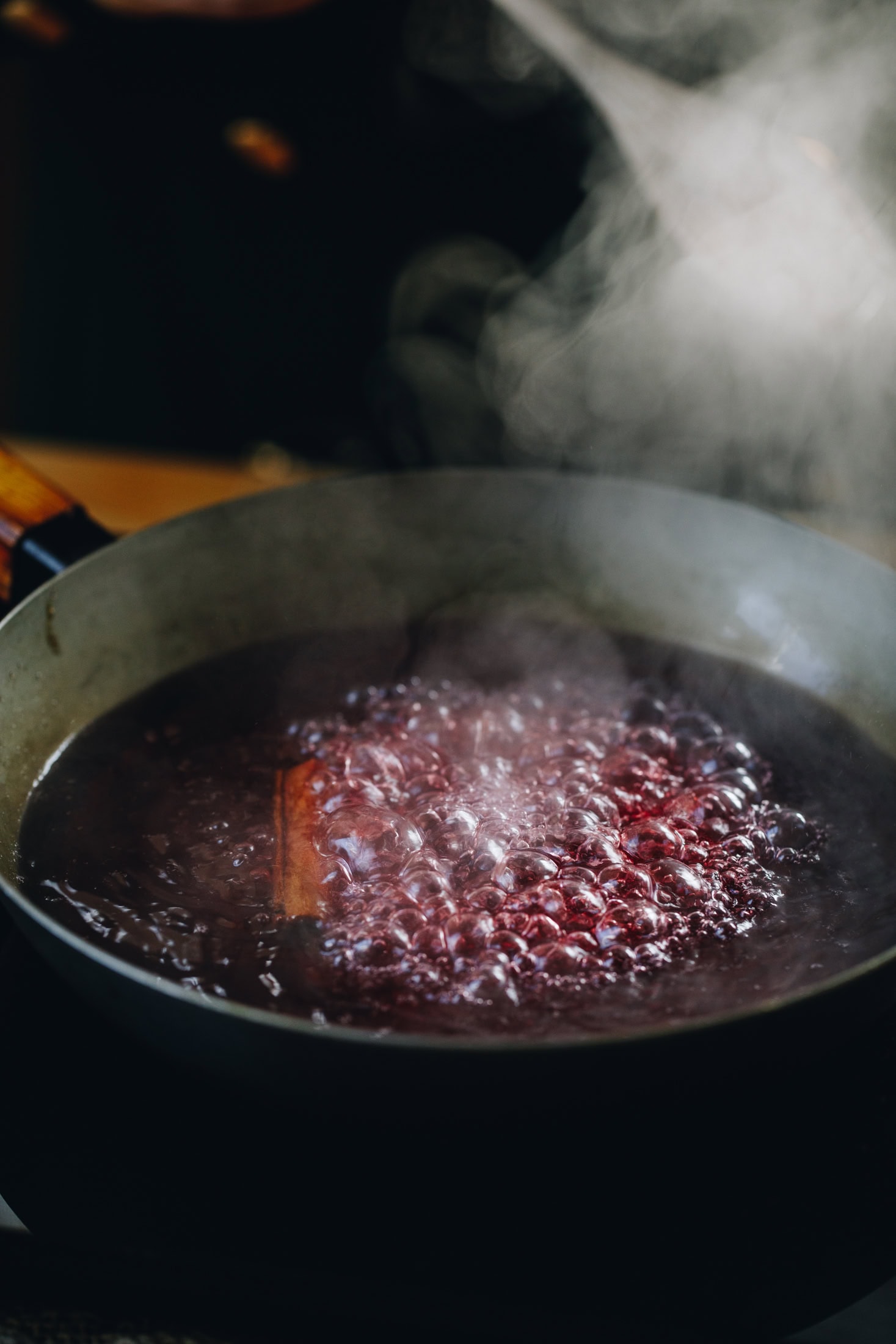 In a frying pan cranberry juice is boiling in a pan with a cinnamon stick on it. There is steam coming out.