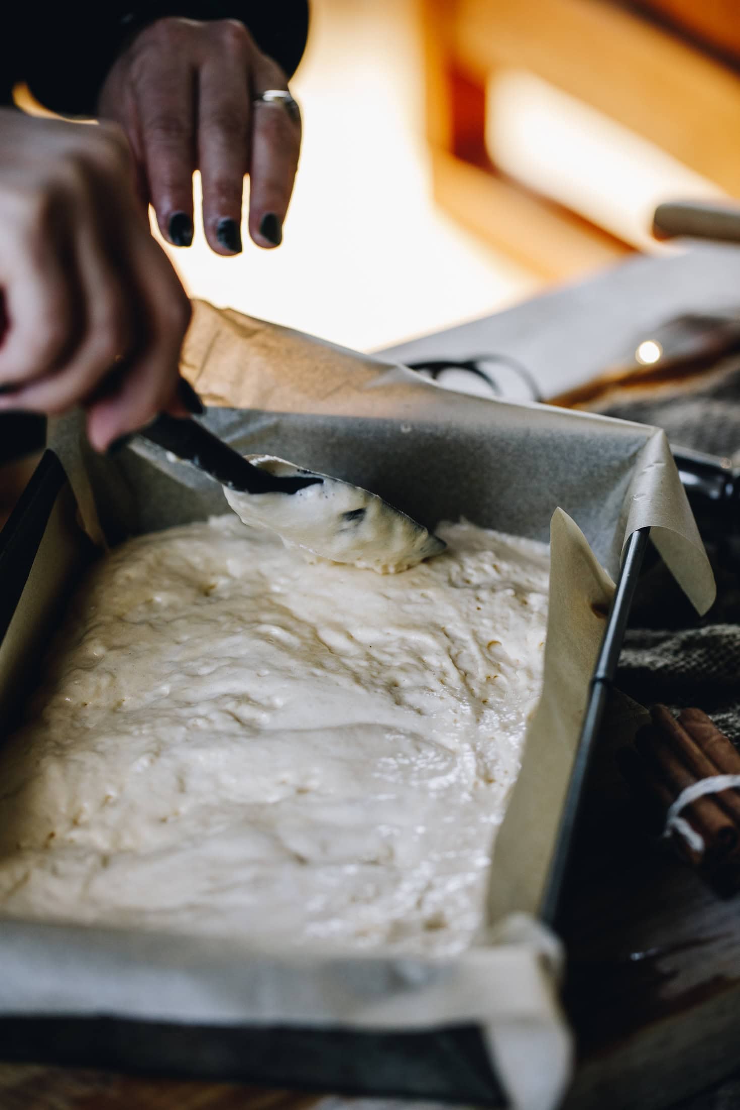 In a baking tin is unbaked sponge mixture for the mini berry trifles. The mixture is being smoothed out on a wooden table.