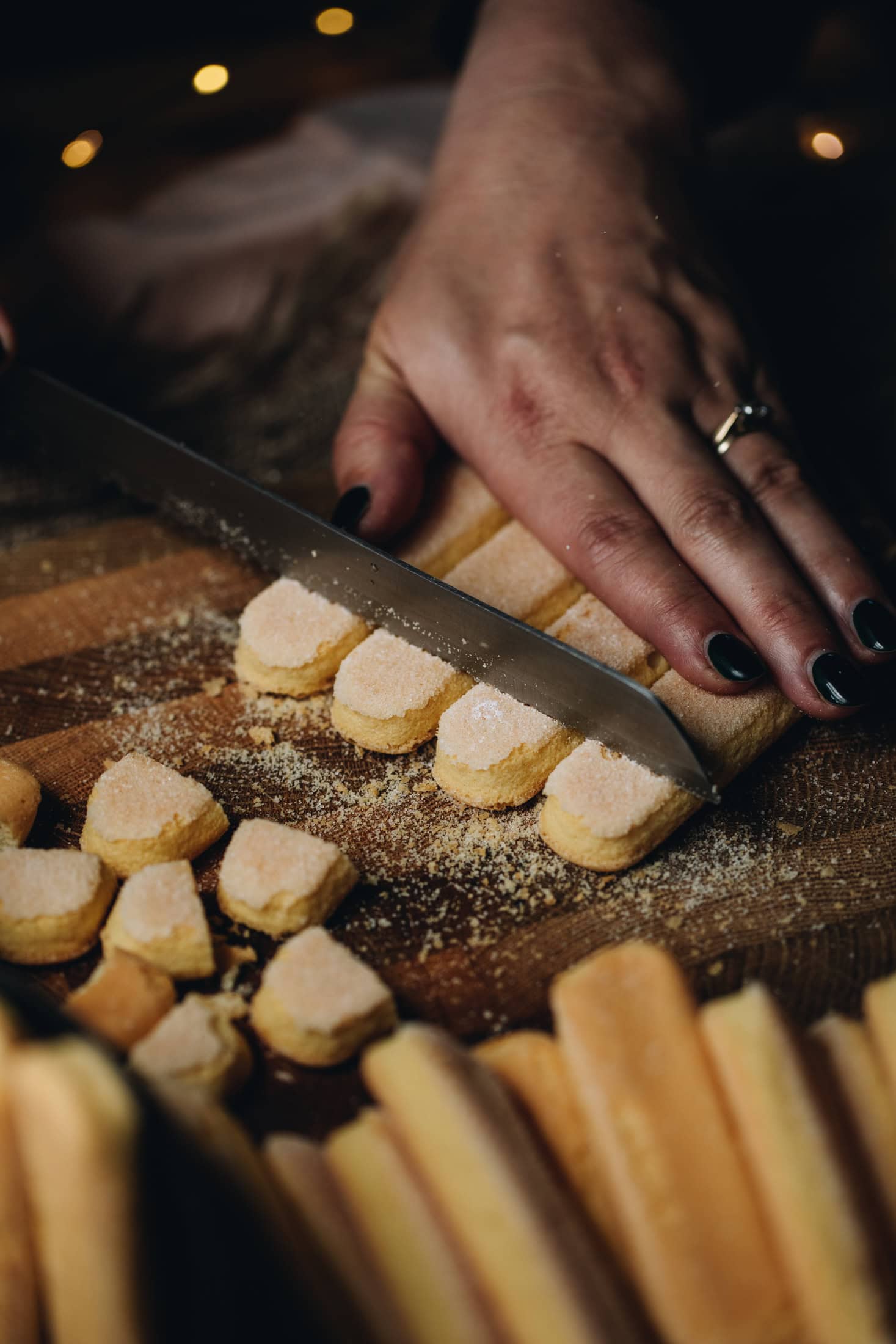 On wooden board hands are cutting the edge off Lady Finger biscuits with a knife. 