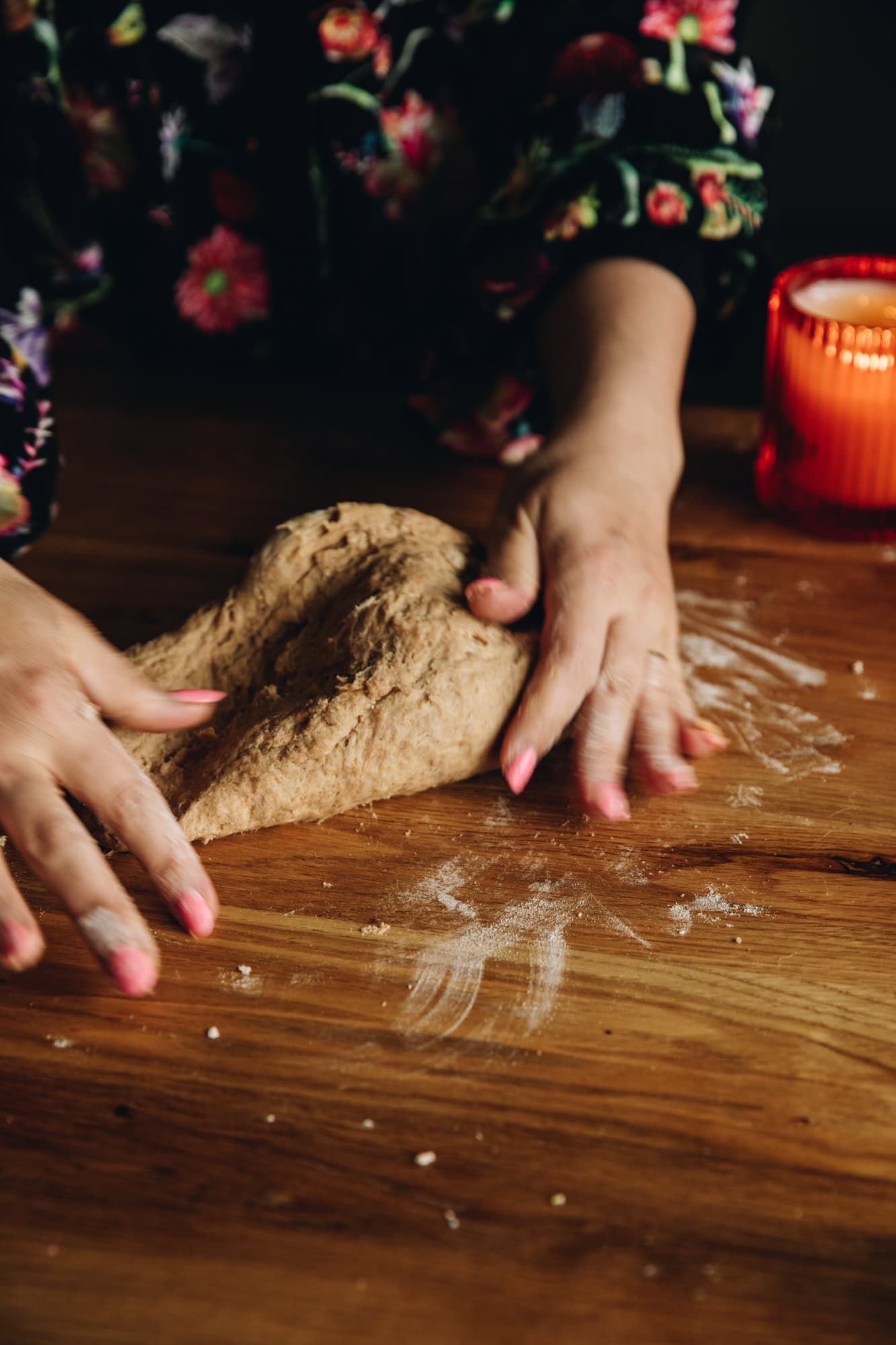 On a floured wooden table two hands are kneading a heavily spiced bread dough. 