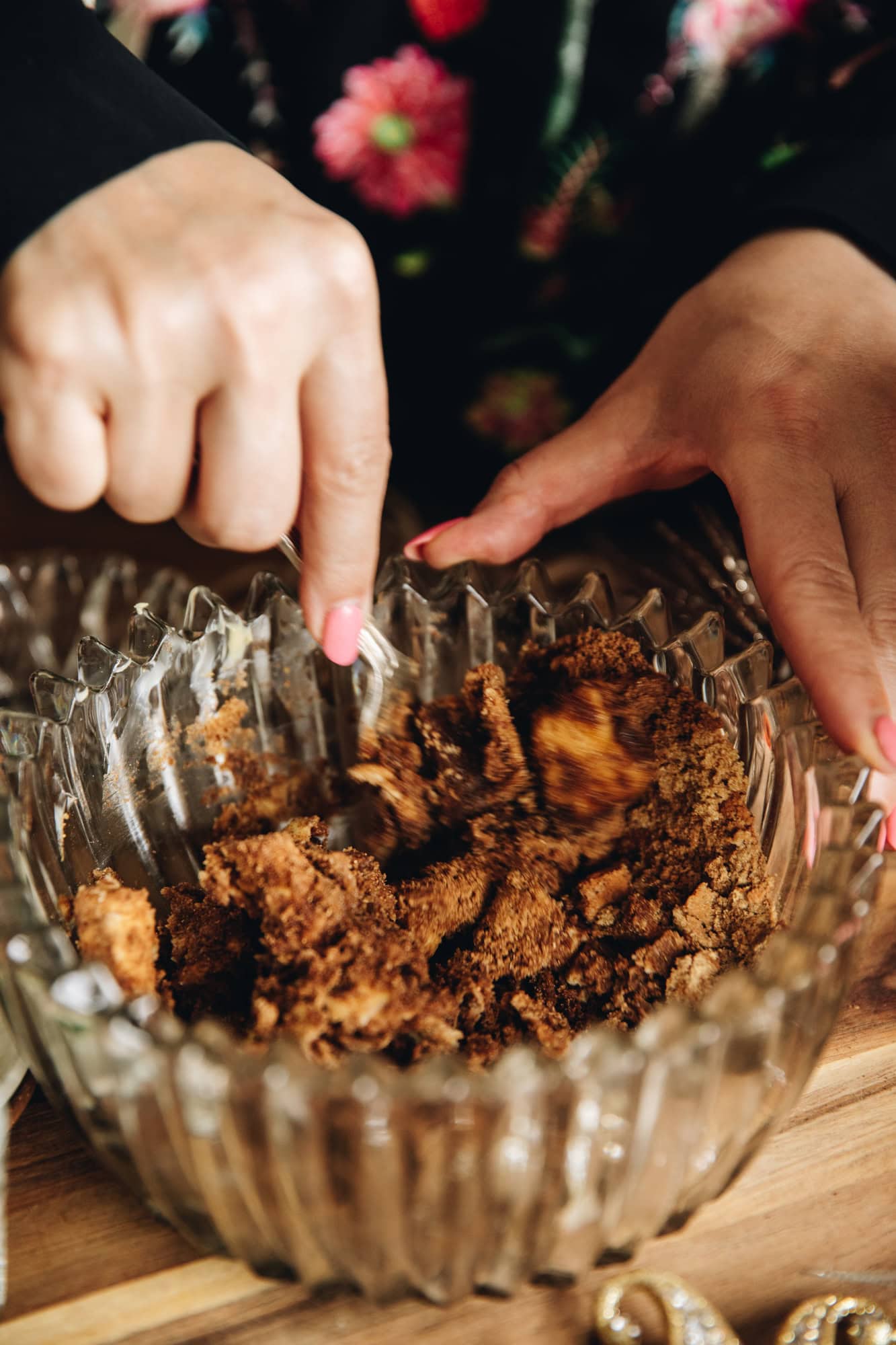 A glass vintage bowl is sitting on a wooden board. In the bowl butter, sugar and spices are being stirred with a fork. 