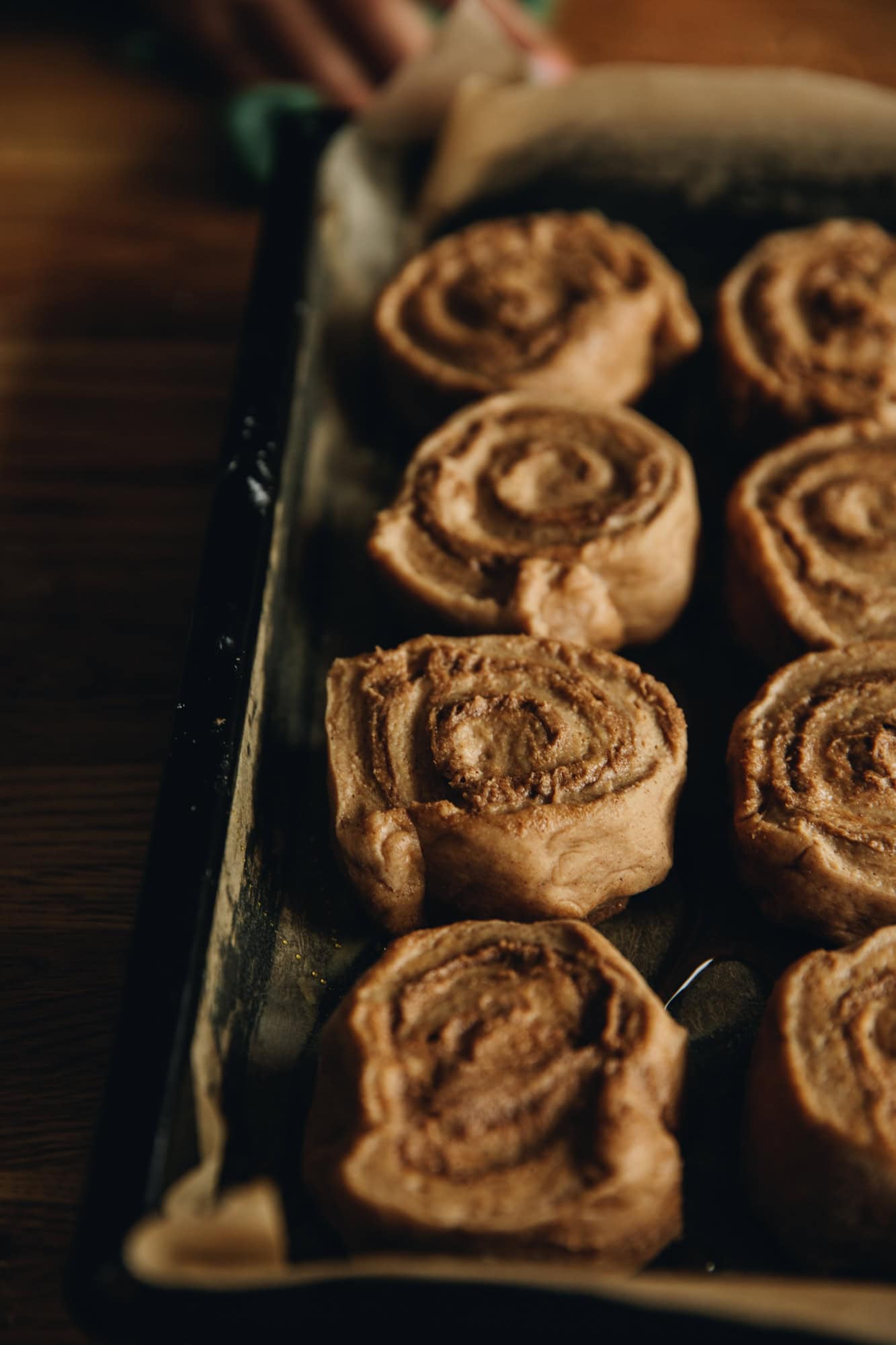 Unbaked sticky gingerbread scrolls are on a black tray lined with baking paper. They are sitting on a wooden table. 
