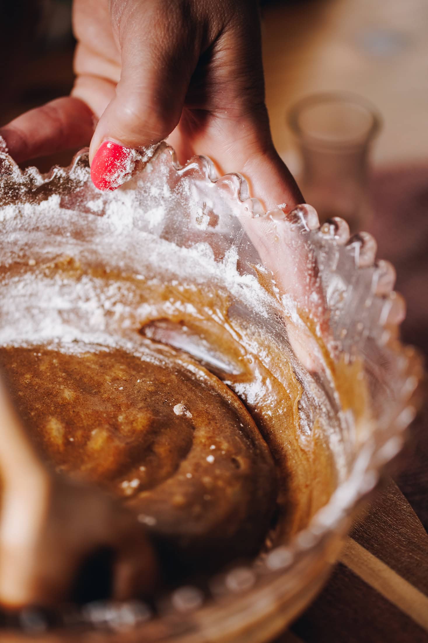 A close up of the brandy snap mixture is in a purple vintage bowl. It is being stirred with flour around the edge. It is on a wooden table.