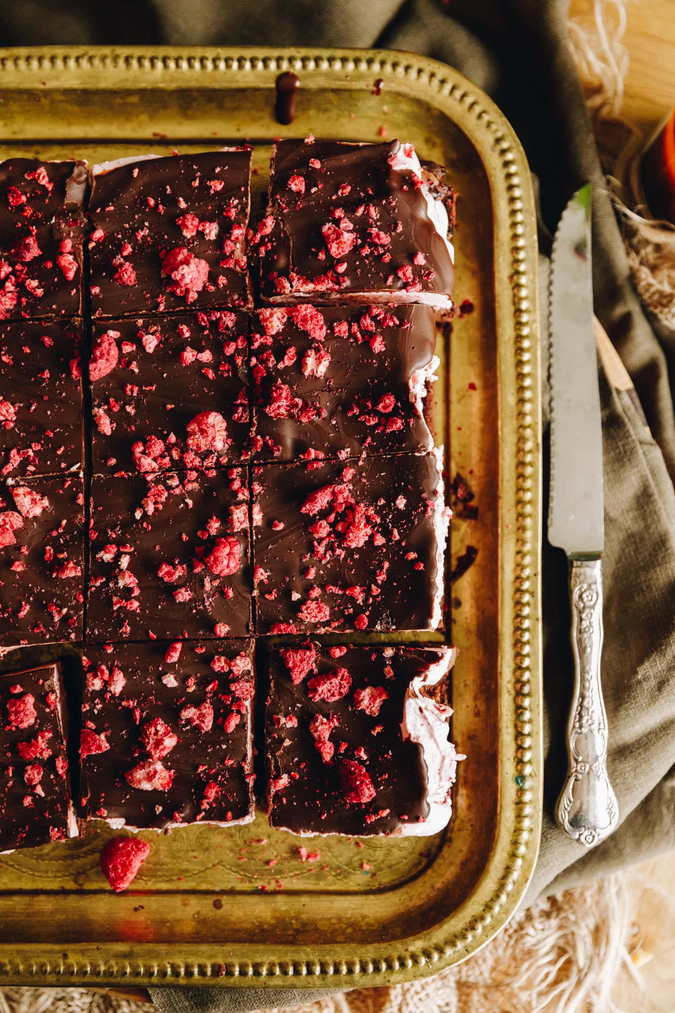 Sliced chocolate raspberry brownie with raspberry marshmallow topping, dark chocolate, and freeze-dried raspberries on a gold tray.
