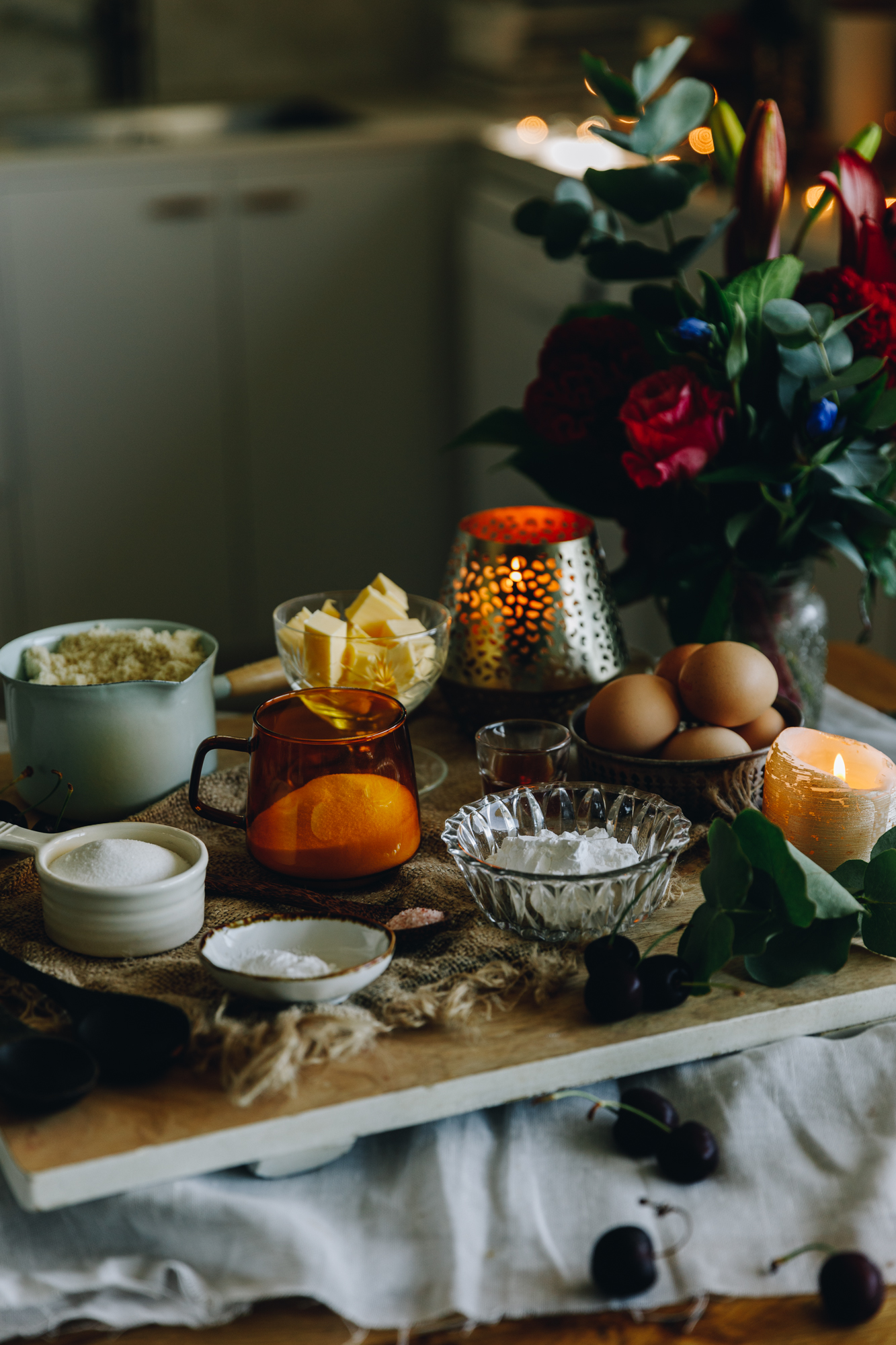 Ingredients are in different vintage bowls and are sitting on a wooden board on top of wooden table There is a bunch of flowers next to the ingredients.