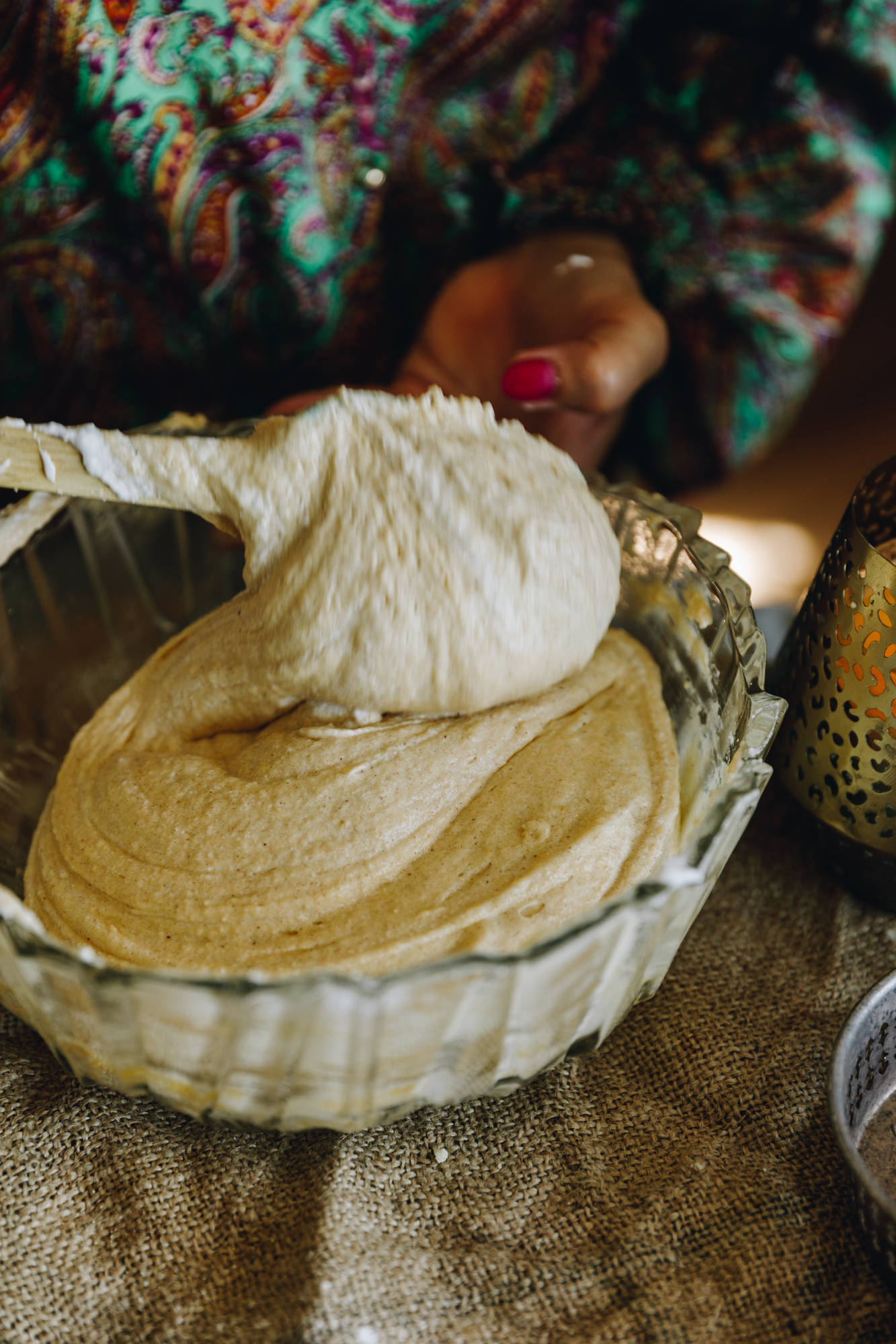 In a glass vintage bowl egg whites are being folded into and almond cake mixture. It is sitting on top a rustic piece of fabric.