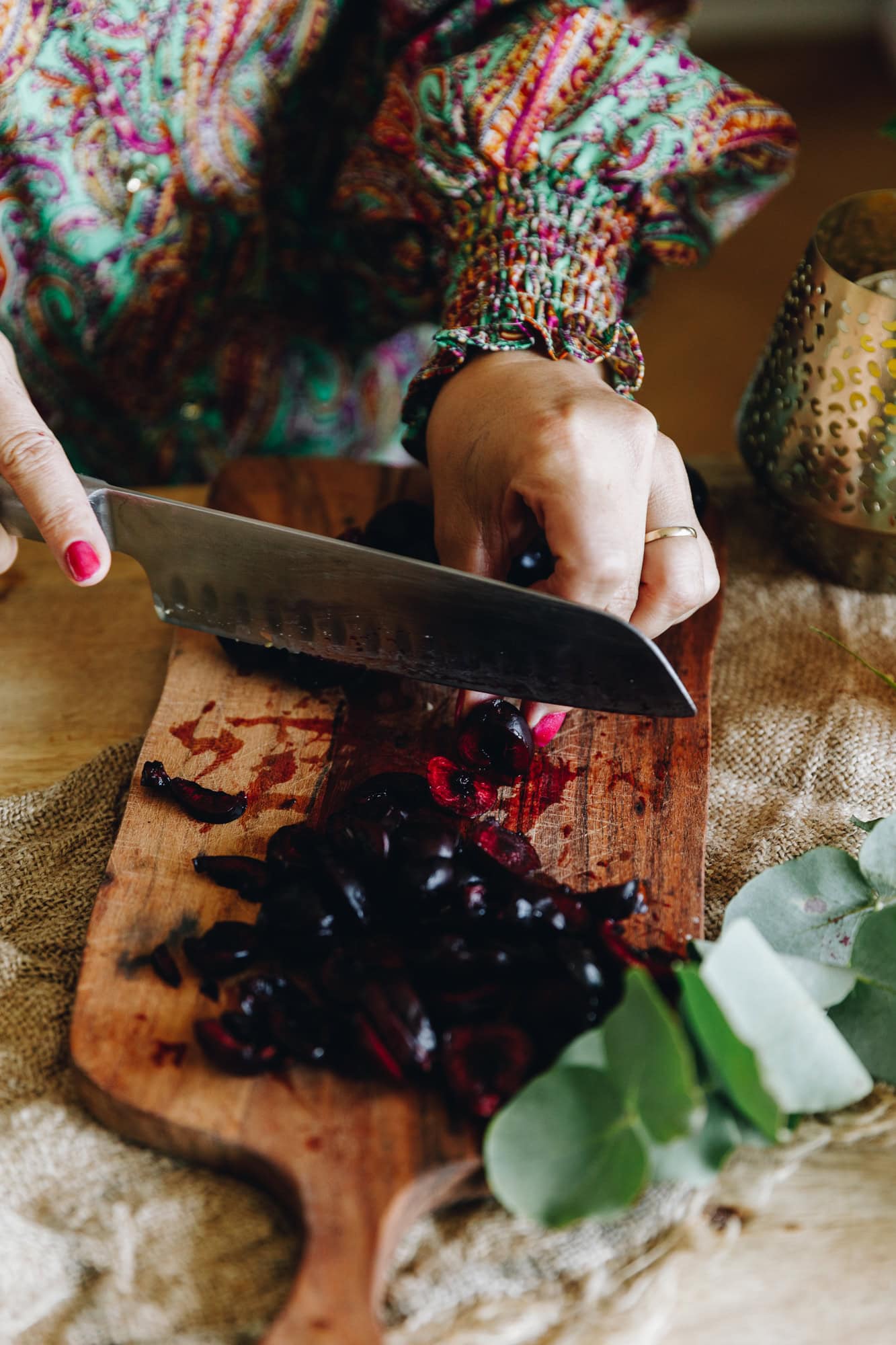On a wooden chopping board is fresh cherries being sliced in to pieces. It is on a wooden table.  