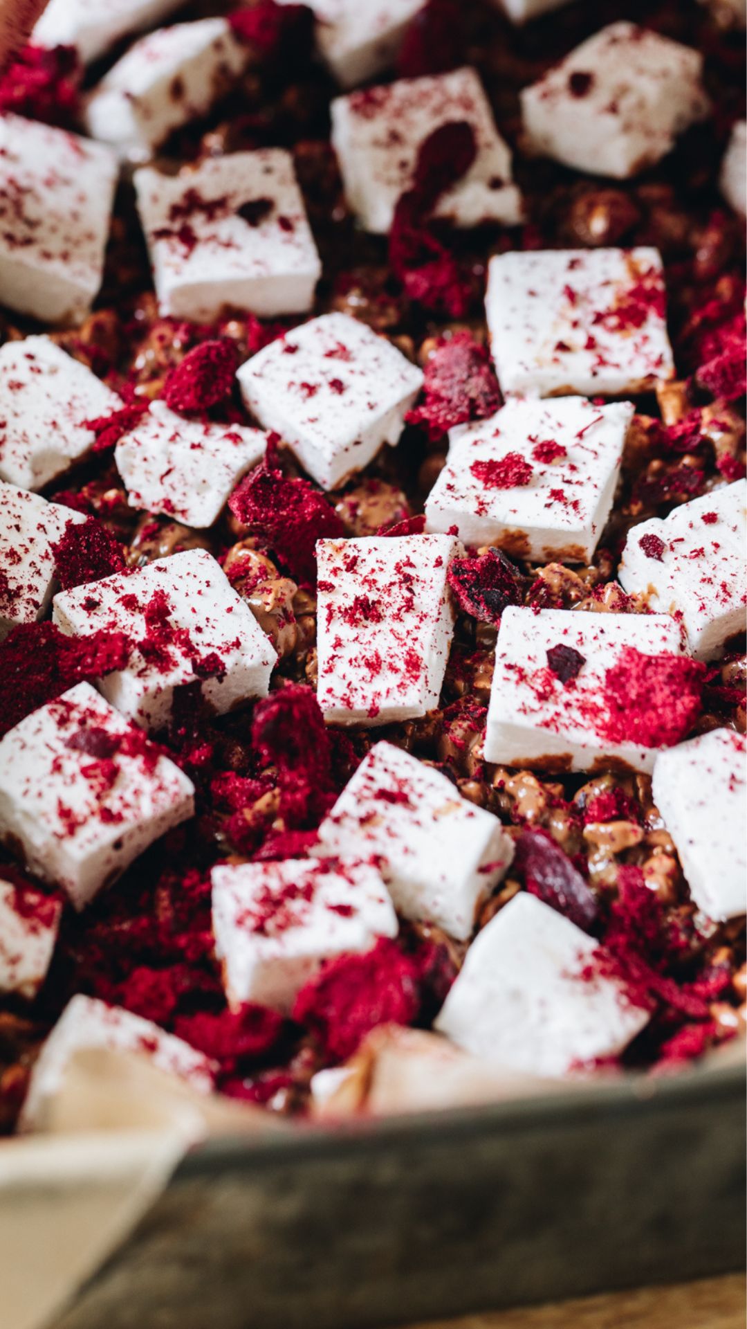 In a baking tray line d with baking paper is easy homemade vanilla marshmallow that has been cut in to squares and has freeze-dried plums sprinkled over top of it. 