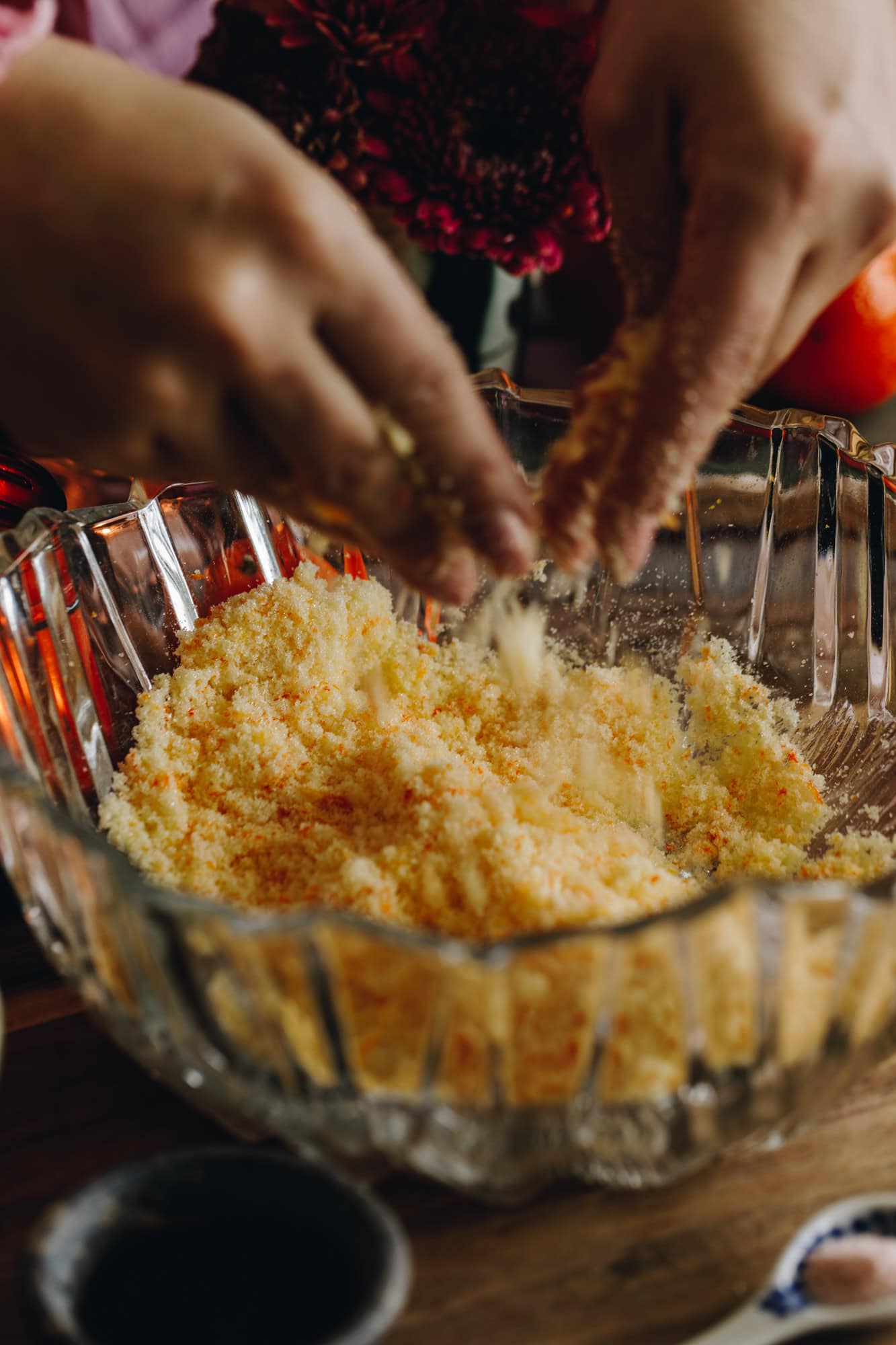The sugar and mandarin zest is being rubbed together with two hands, the action shows the sugar being rubbed and dropping in to the glass bowl.