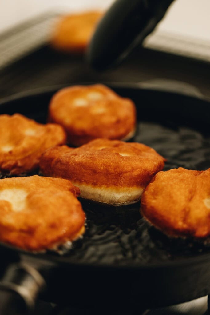 The Light and Fluffy Fry Bread is being fried in the oil in a black cast iron pot. The fry bread is golden on top.