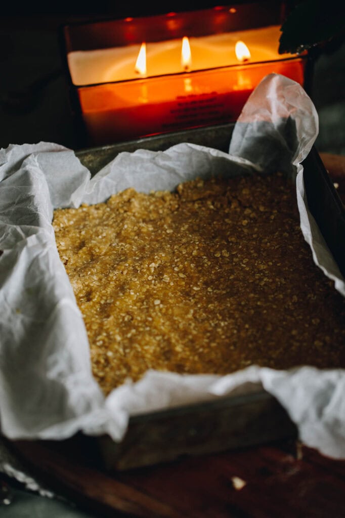 Best Oaty Caramel Slice unbaked base mixture, pressed in to the tin with a large candle in the background.