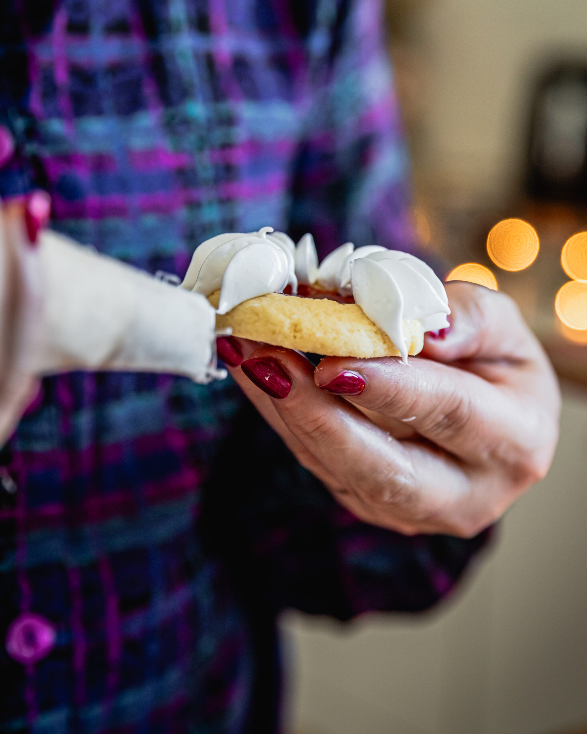 Close up shot of a baked strawberry jam drop being held in a hand. It is being decorated with meringue. 