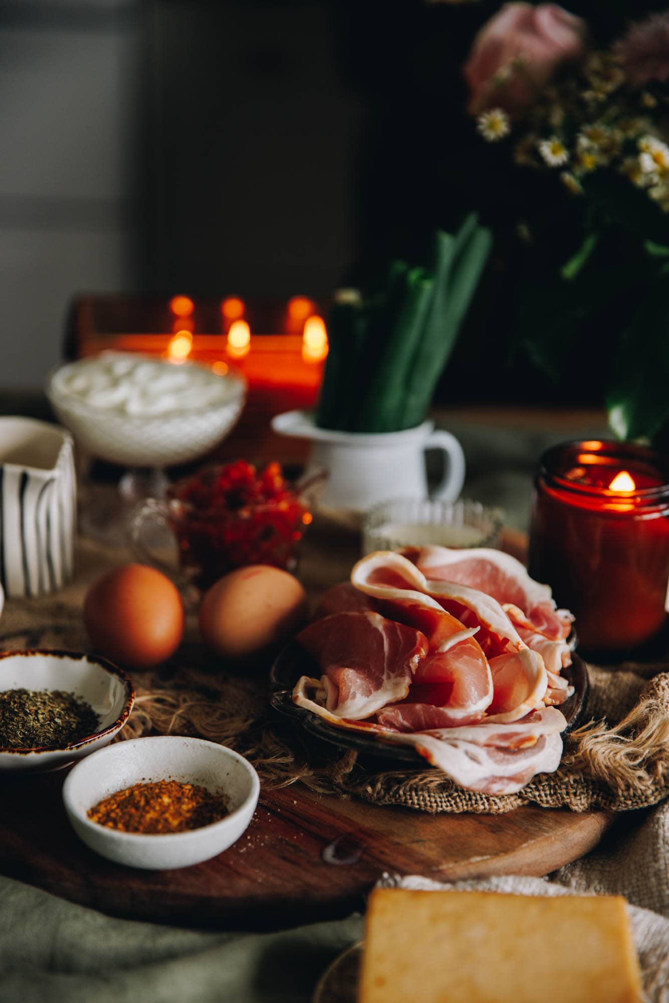 Ingredients are on a wooden board in vintage cups, spoons and bowls. Bacon, eggs and spring onions can be seen.