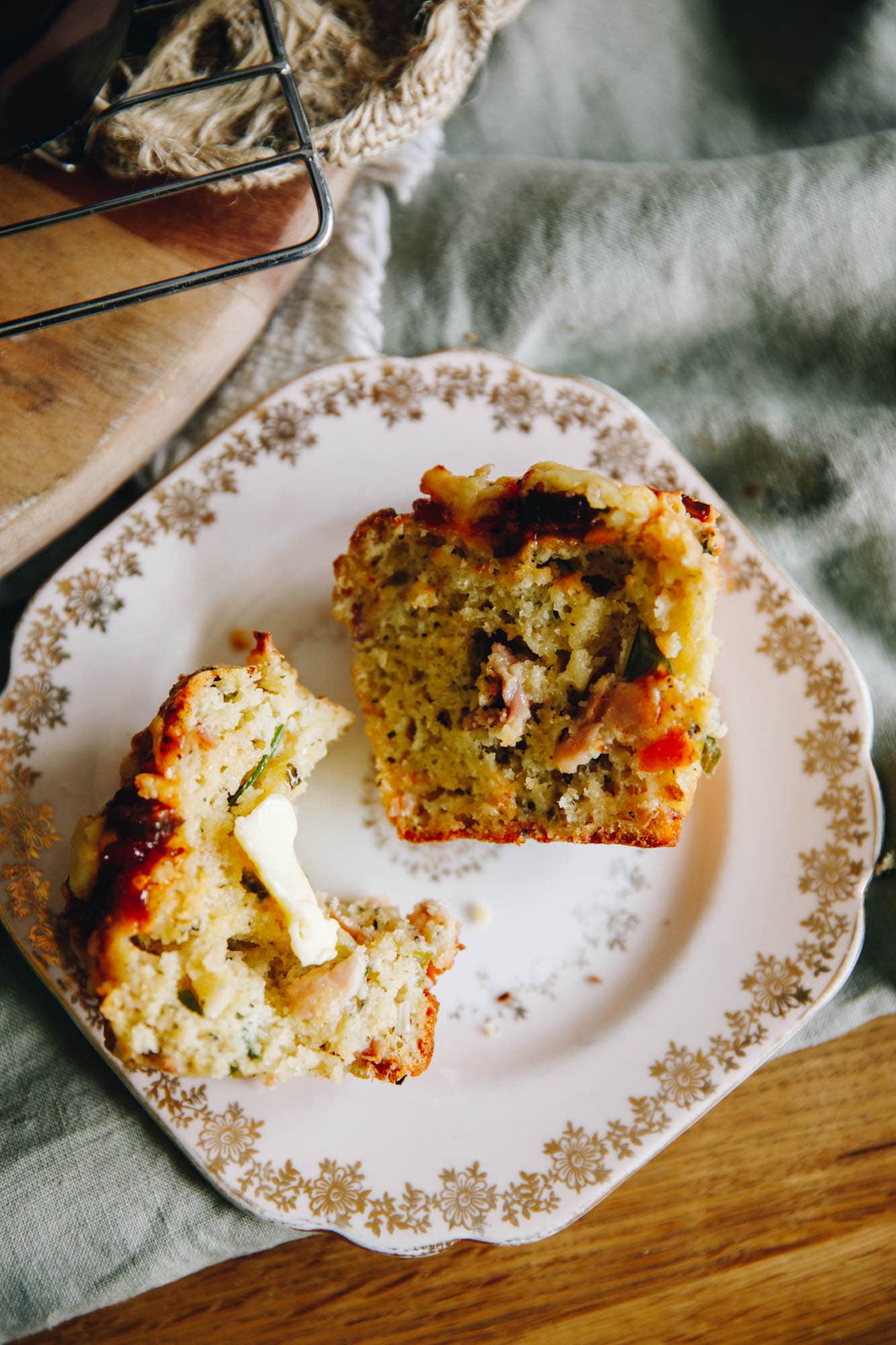 A cheesy bacon savoury muffin is cut open and is on a small pink plate. One side shows the inside and the other has a bite out of it with butter melting on to it.
