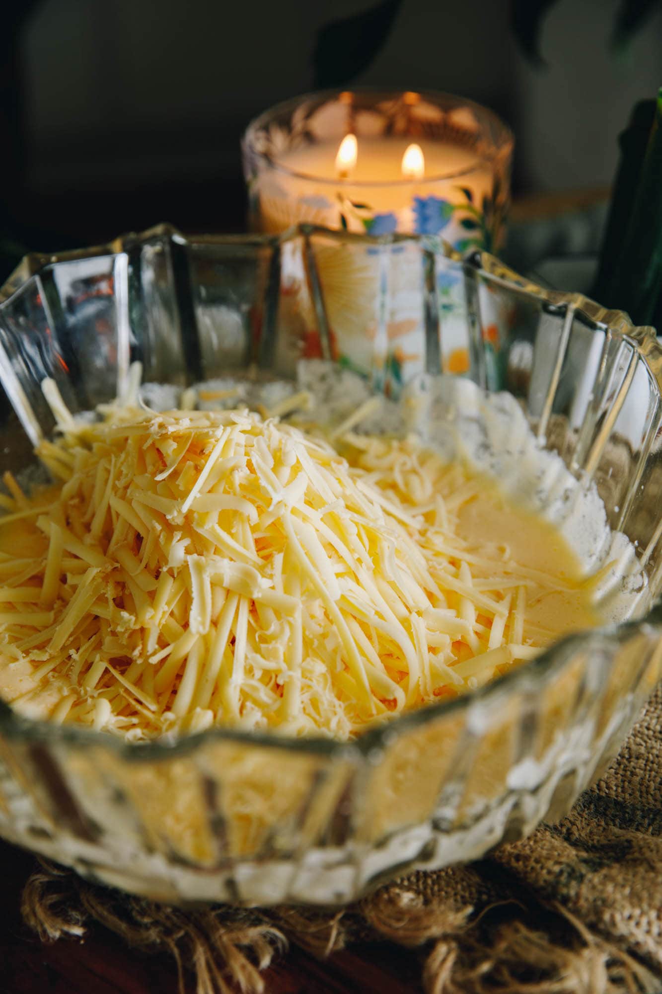 A glass bowl is filled with an egg mixture and is pile high with grated cheese.