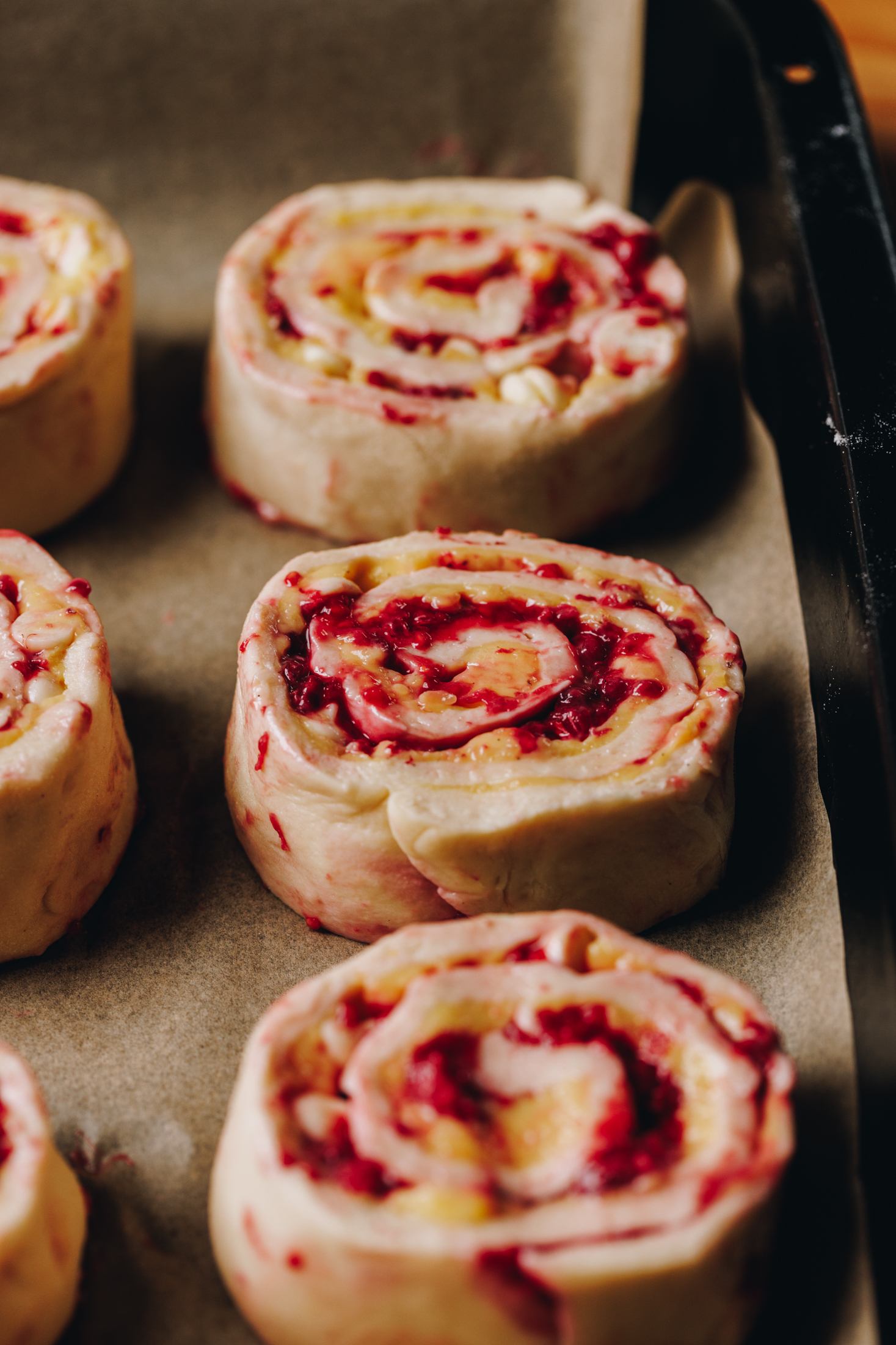 In a black tray lined with brown baking paper are three rolled and unbaked scrolls.