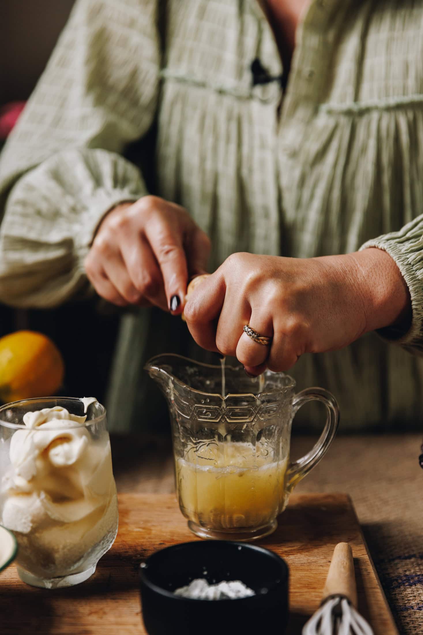 On a wooden board is a vintage glass jug and Naomi Toilalo is squeezing lemon juice out with a wooden juicer. On the chopping board is a glass of creme fraiche.
